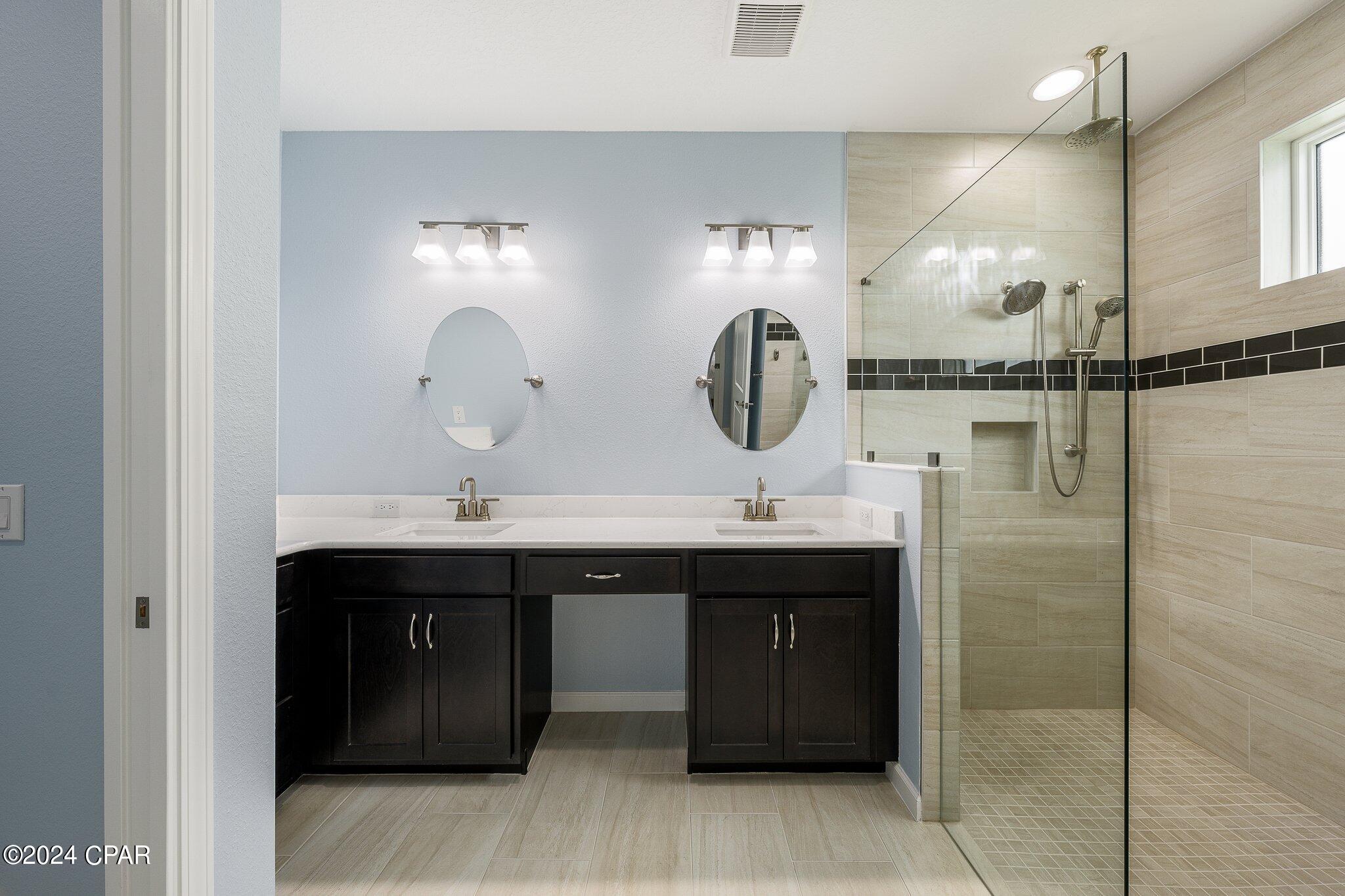 Bathroom with a dark double vanity and a glass-enclosed tiled walk-in shower.
