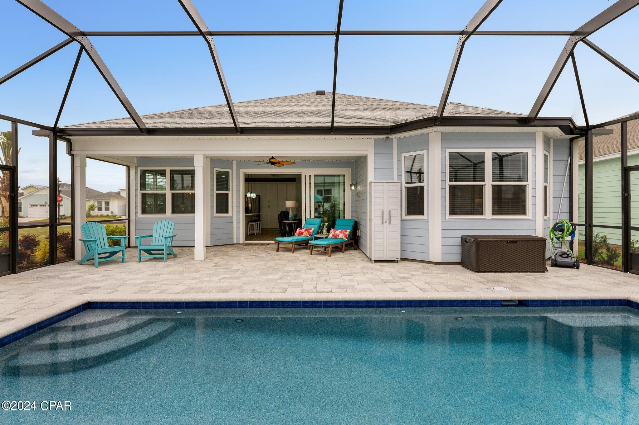 Swimming pool beside a screened, covered patio with turquoise chairs and a light-blue house.