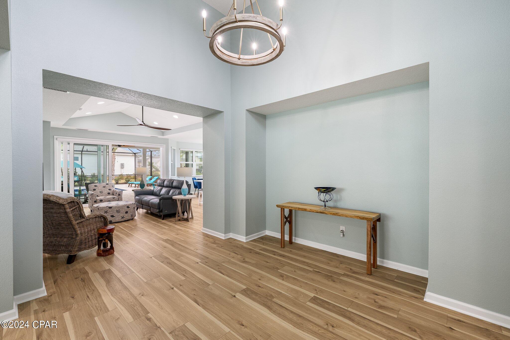 Entryway with wood floors and chandelier opening to a furnished living room and patio doors.