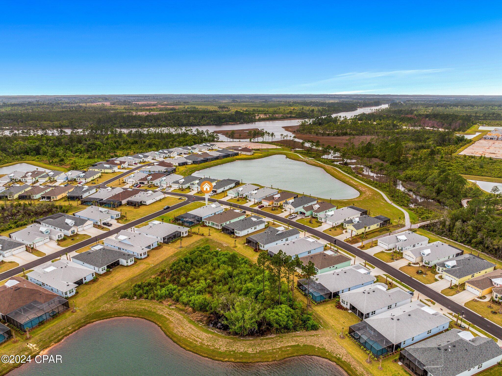 Aerial neighborhood view with the marked home beside a large pond and a winding river beyond.