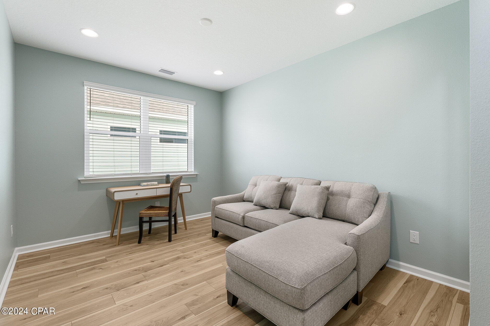 Sitting room with a gray chaise sectional and desk beneath a window with blinds.