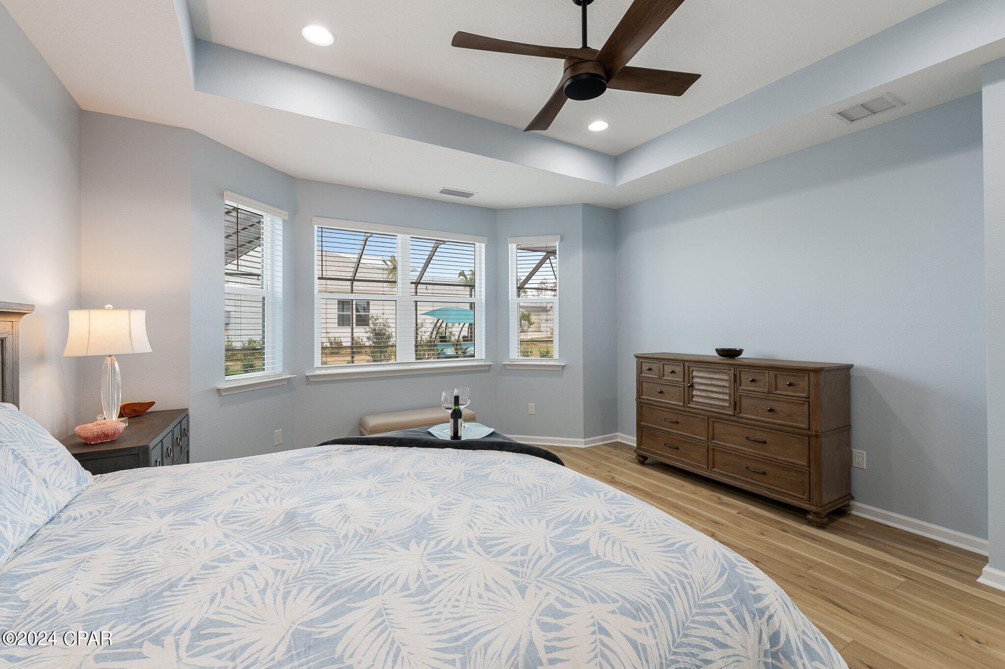 Furnished bedroom with pale blue patterned bedding, three windows, and a dark wood dresser.