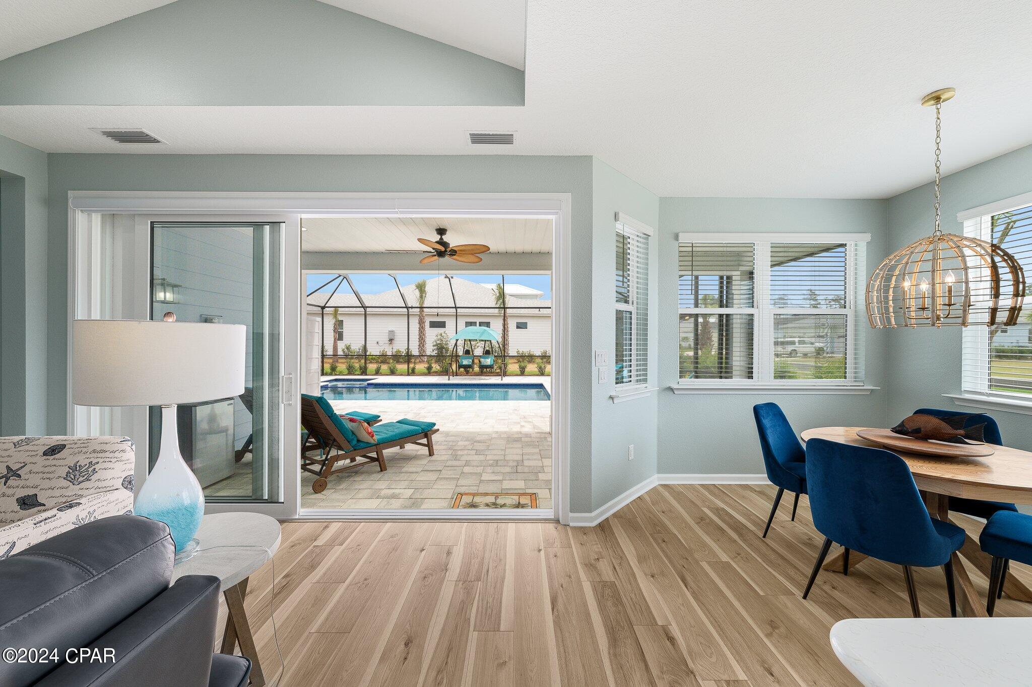 Open-plan living and dining room with blue chairs and sliding doors overlooking a screened patio pool.