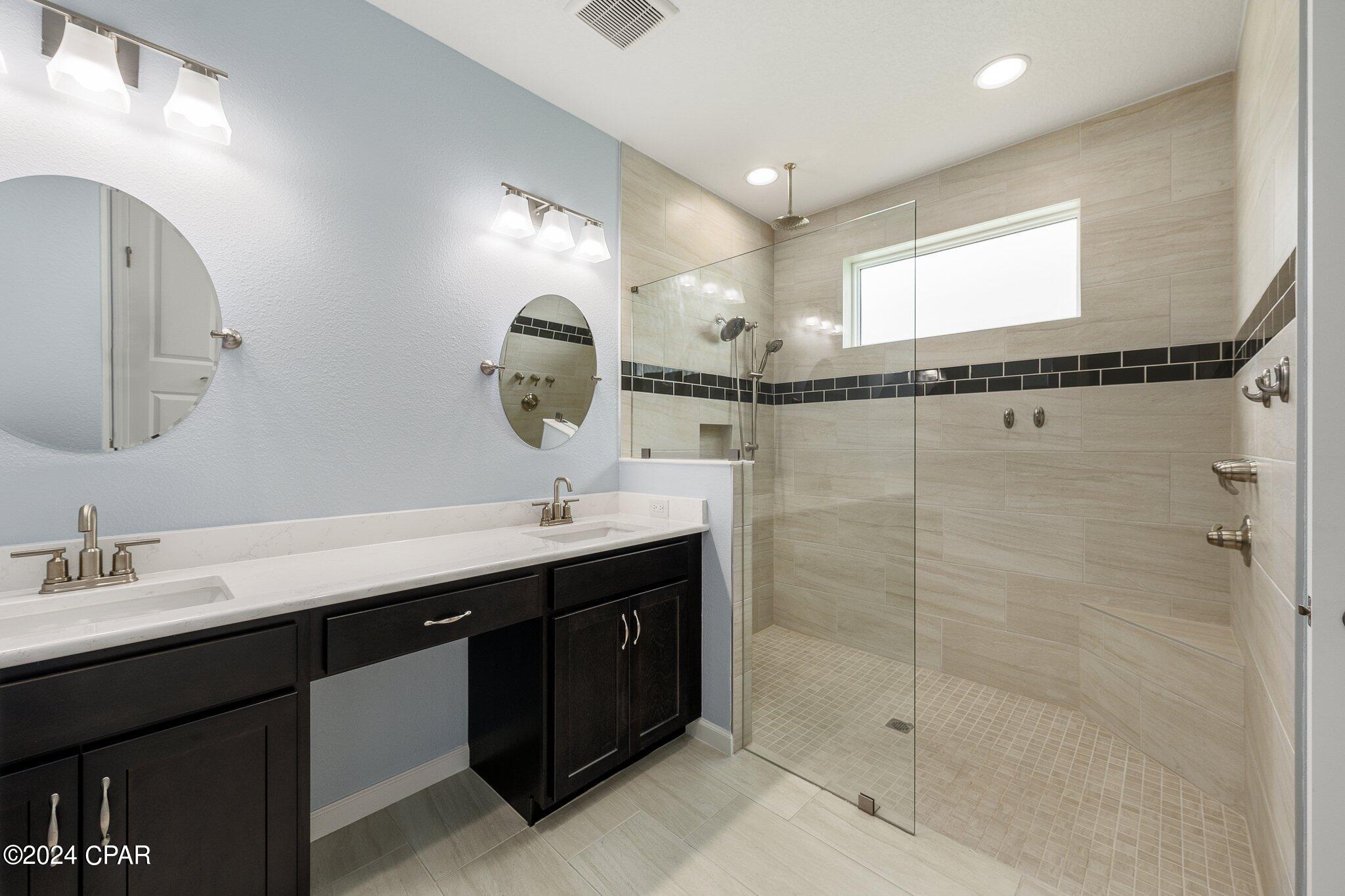 Bathroom with dark double vanity and a spacious glass-enclosed shower with beige tile.