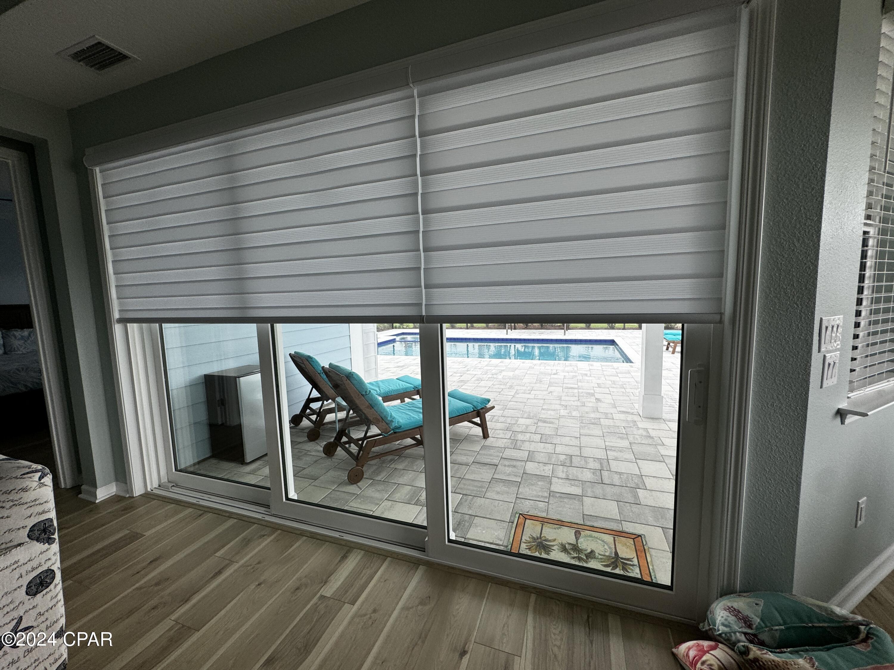Sliding glass doors open onto a tiled pool patio with turquoise lounge chairs.