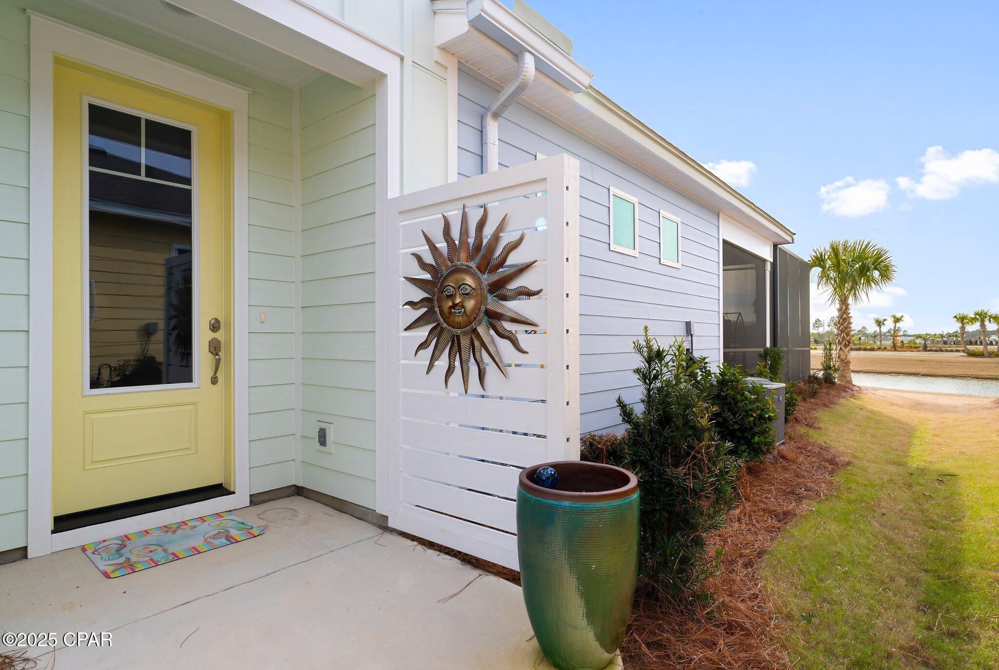 Home entry with a yellow door and sun-decorated screen beside a landscaped yard and water.