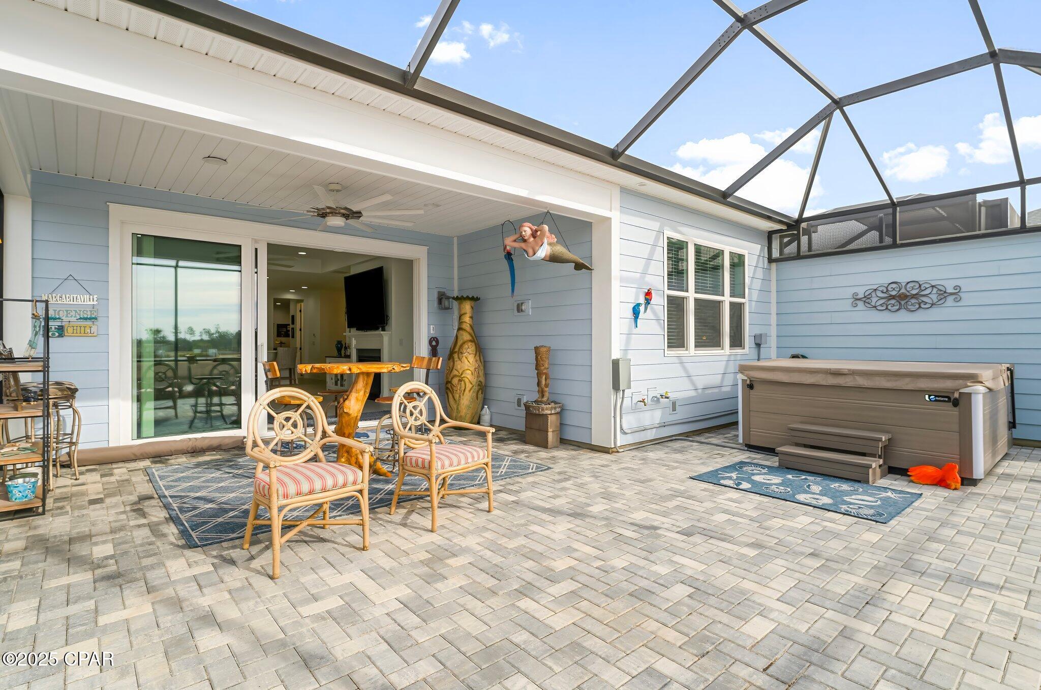 Screened patio with a hot tub, wicker seating, paver flooring, and sliding doors.