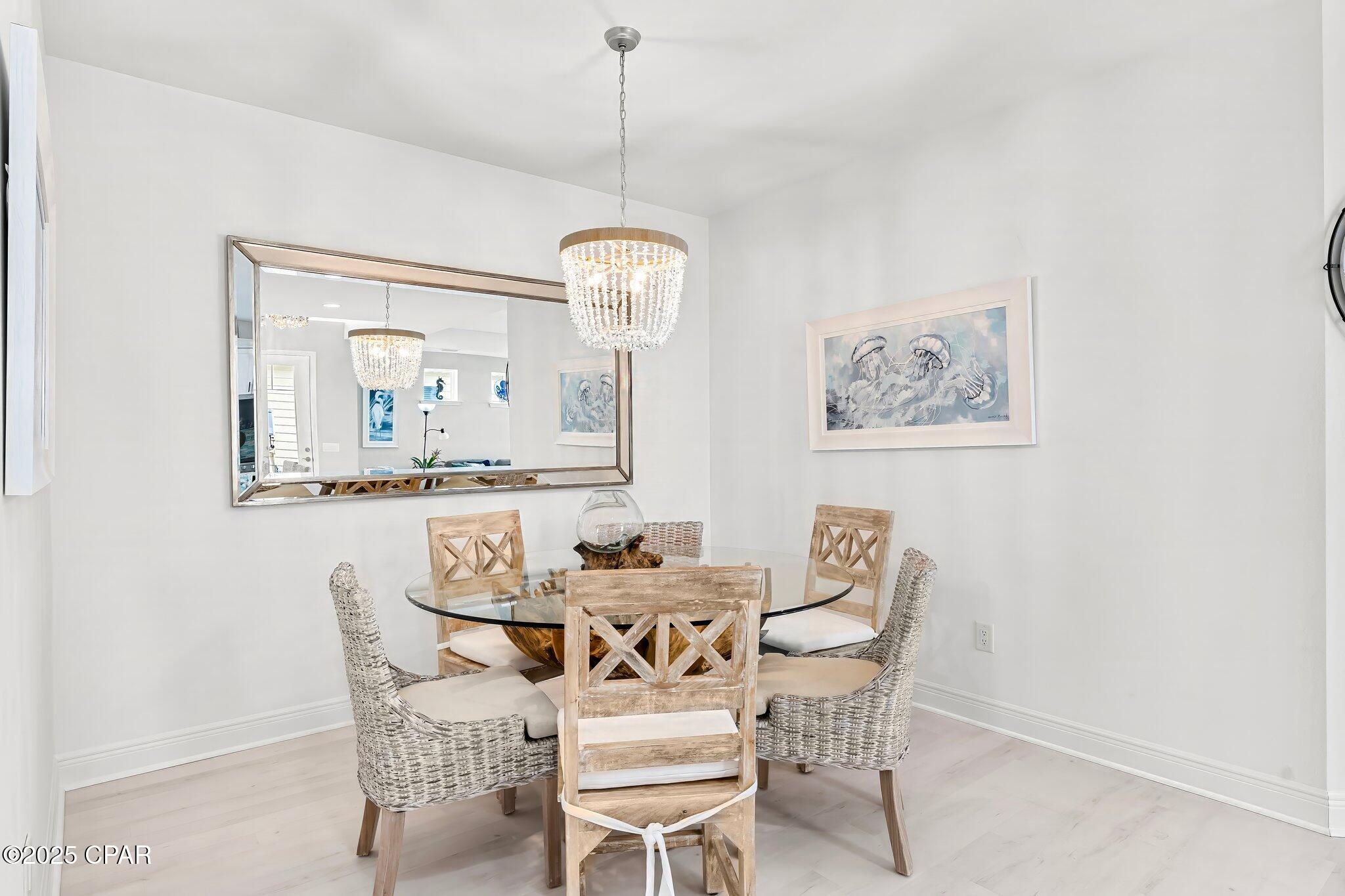 Dining room with a glass-top table, woven chairs, crystal chandelier, and jellyfish artwork.