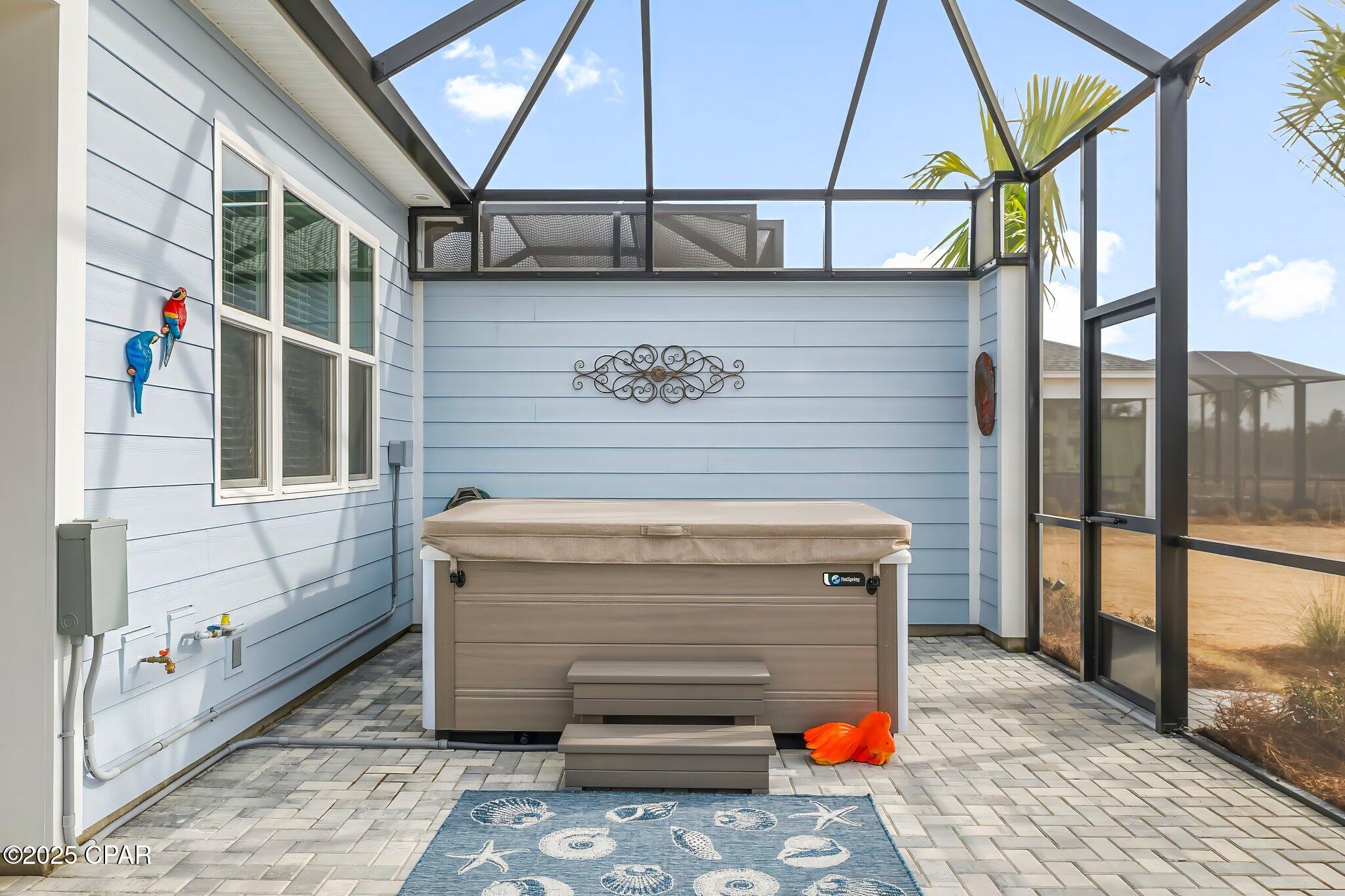 Screened patio with a large hot tub, paver floor, and colorful tropical decorations.