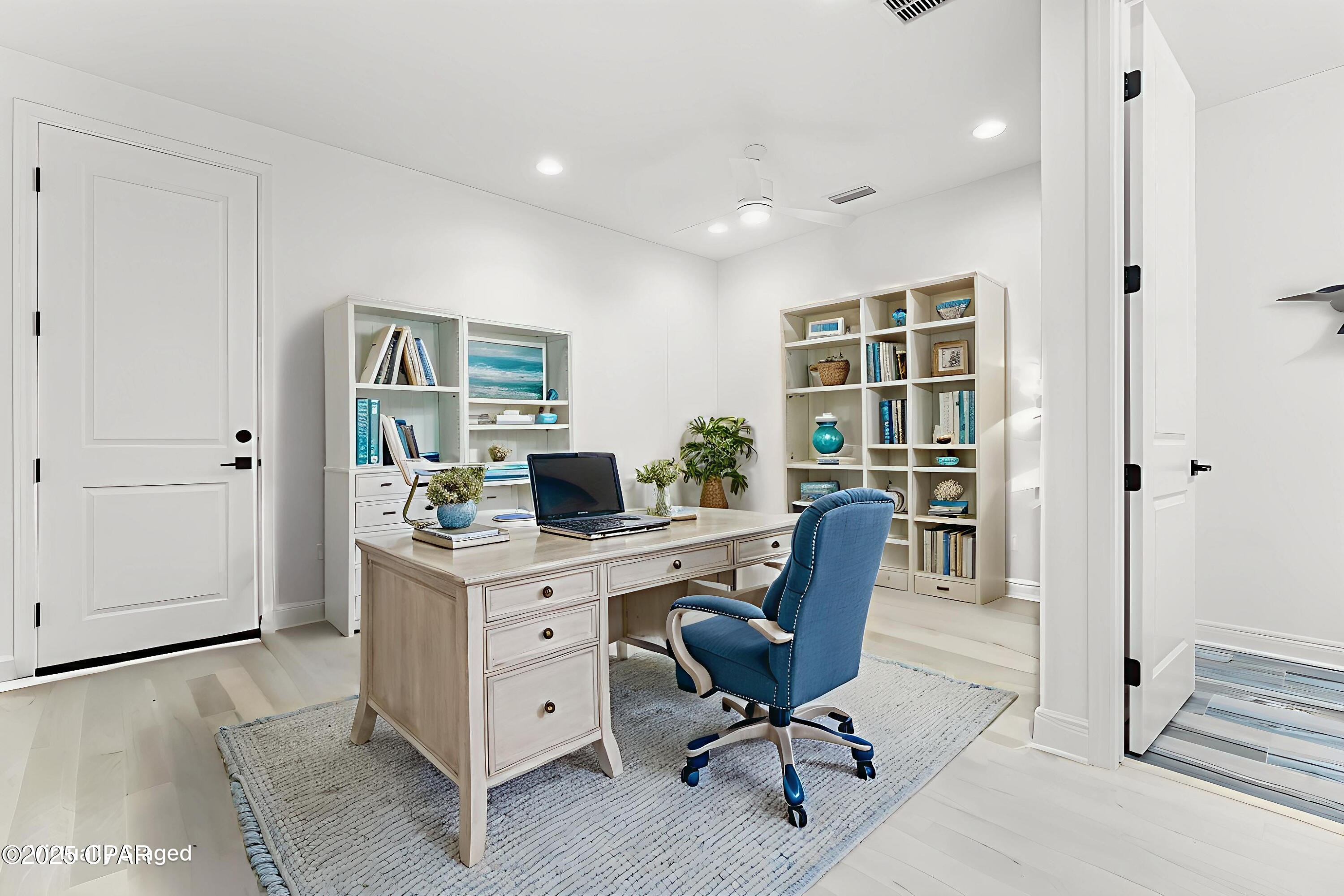 Furnished home office with a light wood desk, blue swivel chair, and built-in bookshelves.