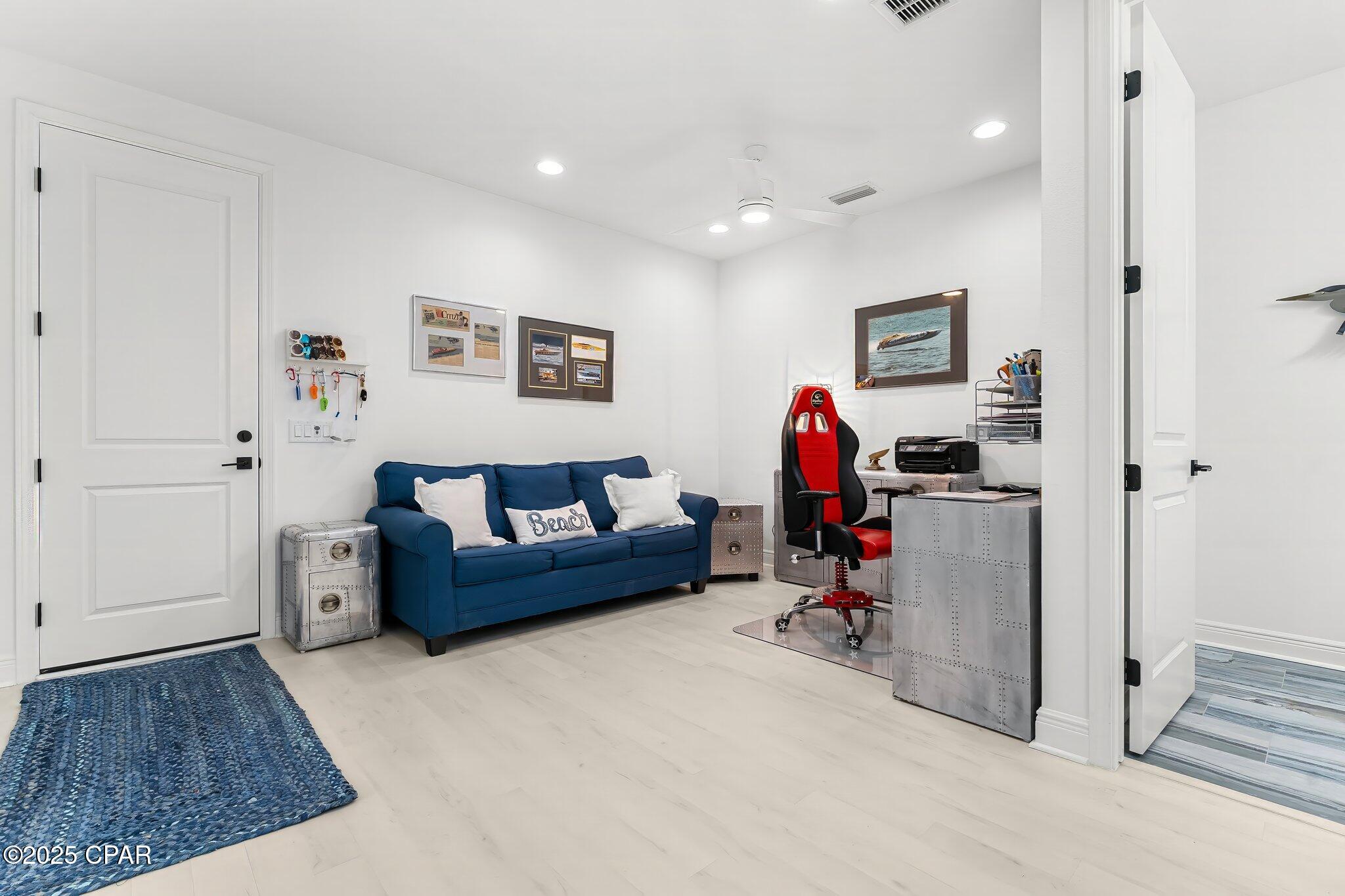 Furnished home office with a blue sofa, red office chair, metal desks, and framed boat pictures.