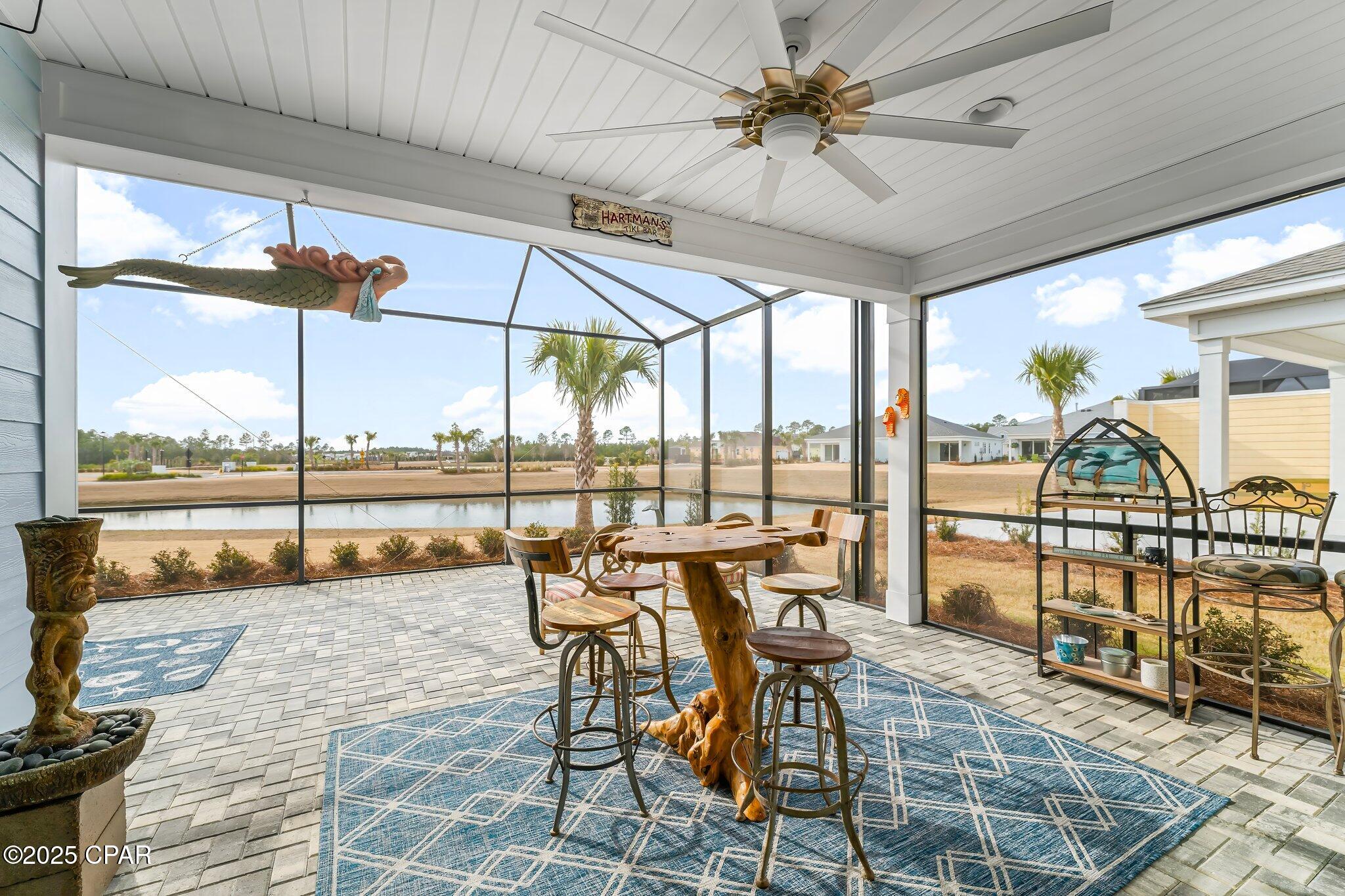 Screened patio with a rustic bar table, blue rug, ceiling fan, and pond view.