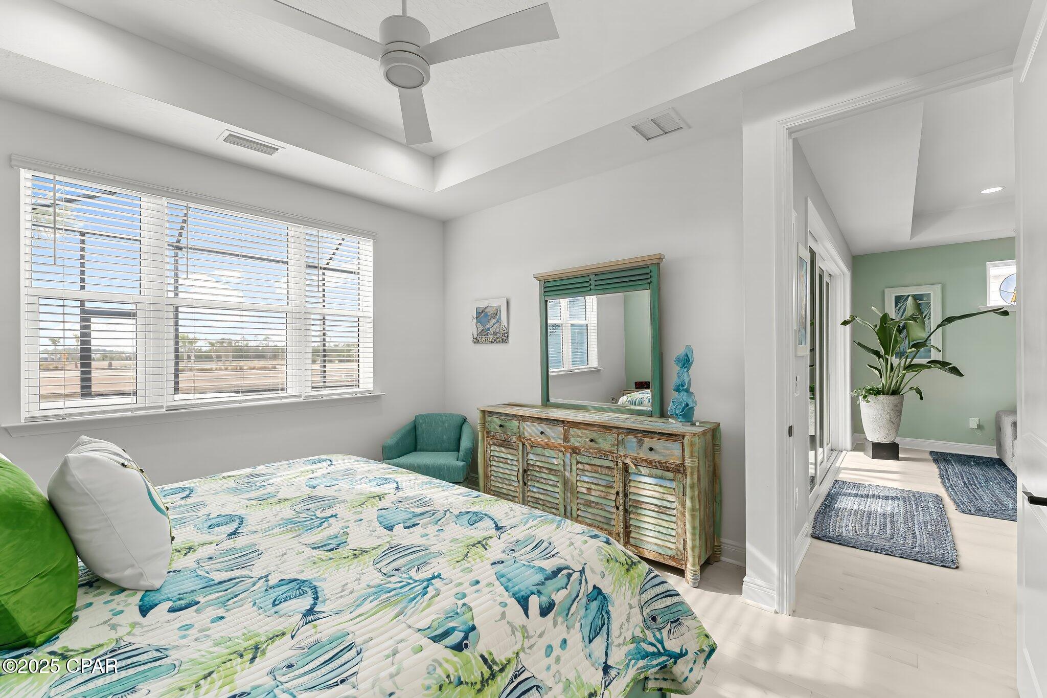 Bedroom with fish-patterned bedding, a distressed turquoise dresser, and a bright hallway beyond.