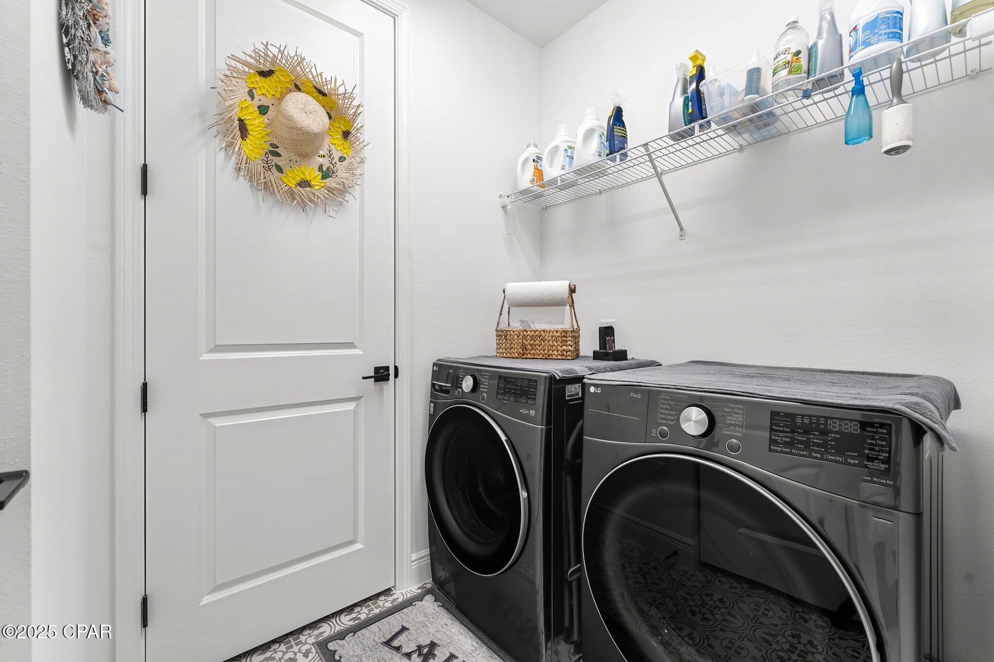 Laundry room with black front-loading washer and dryer beneath a shelf of cleaning supplies.