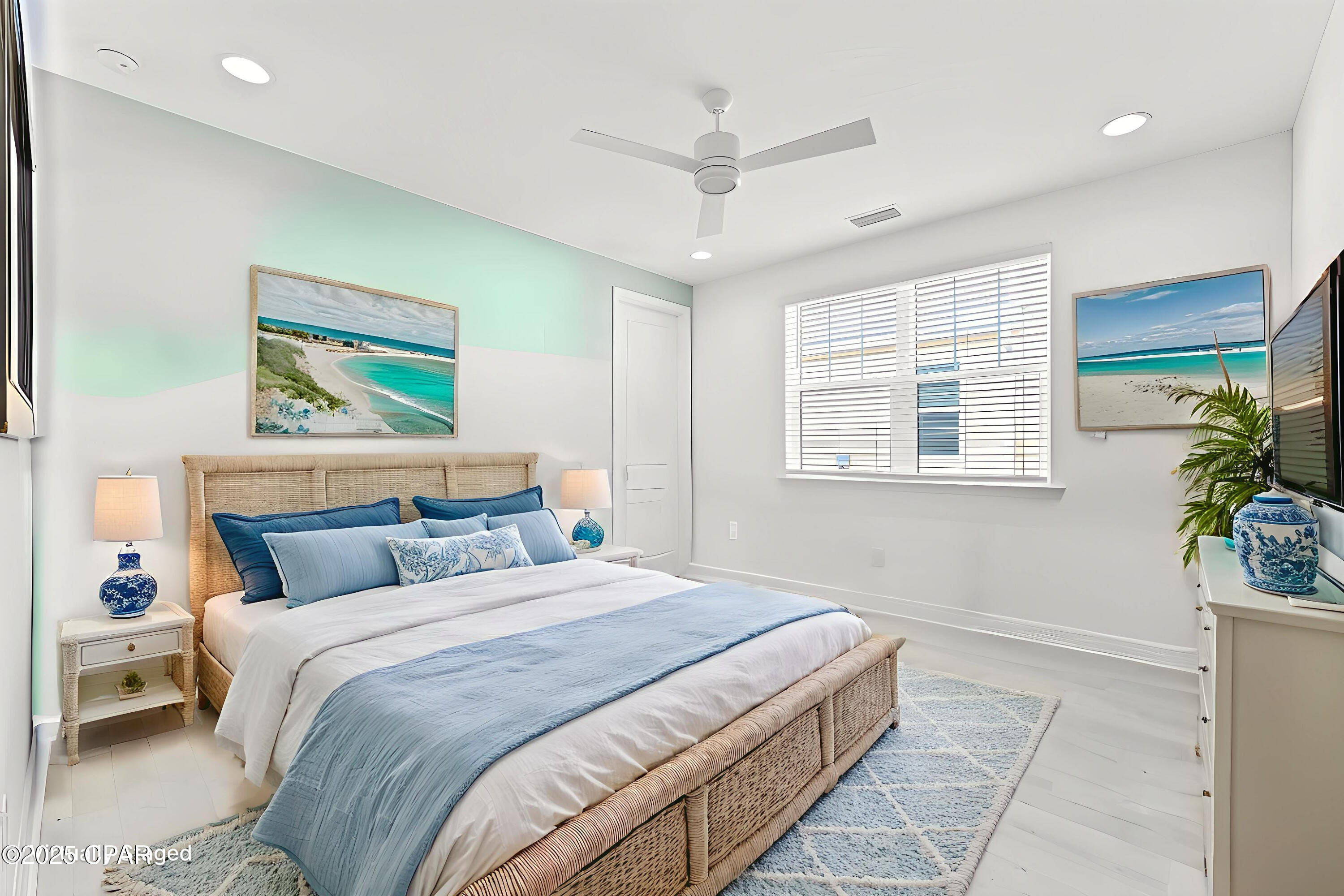 Bedroom with woven bed, blue-and-white bedding, ceiling fan, and beach prints.
