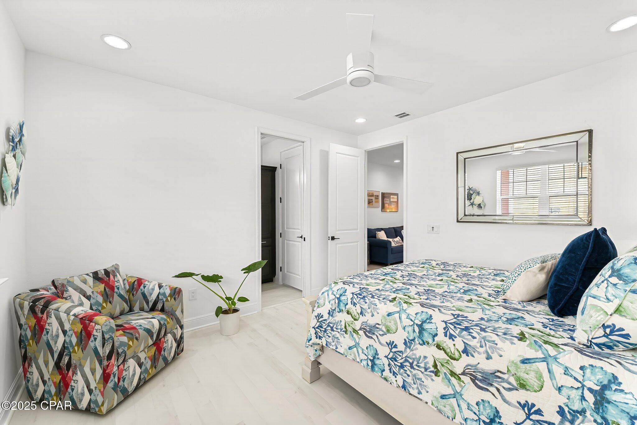 Bedroom with botanical bedding, a colorful patterned armchair, and a large wall mirror.
