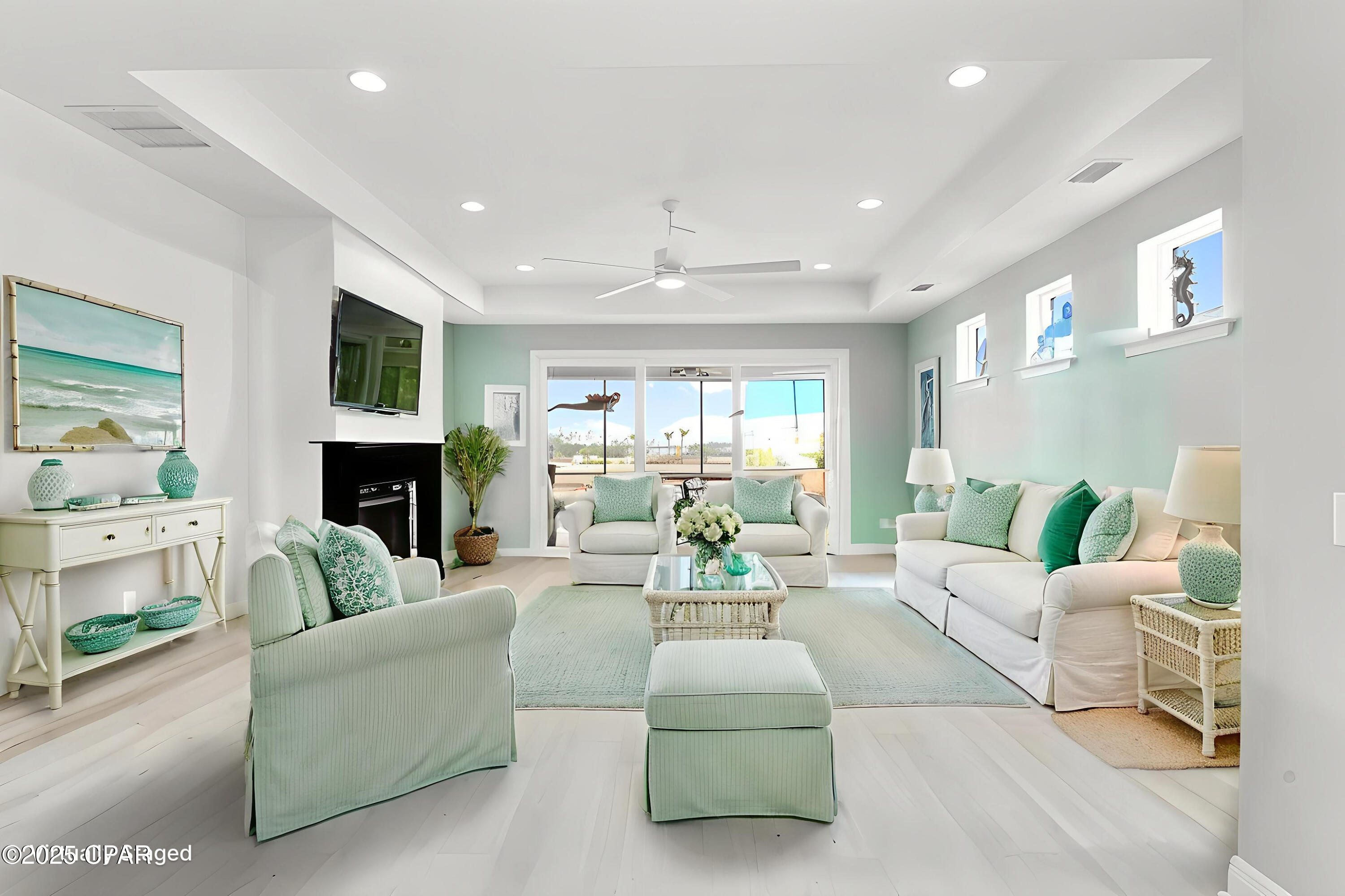 Staged living room with white seating, mint-green accents, a black fireplace, and large glass doors.