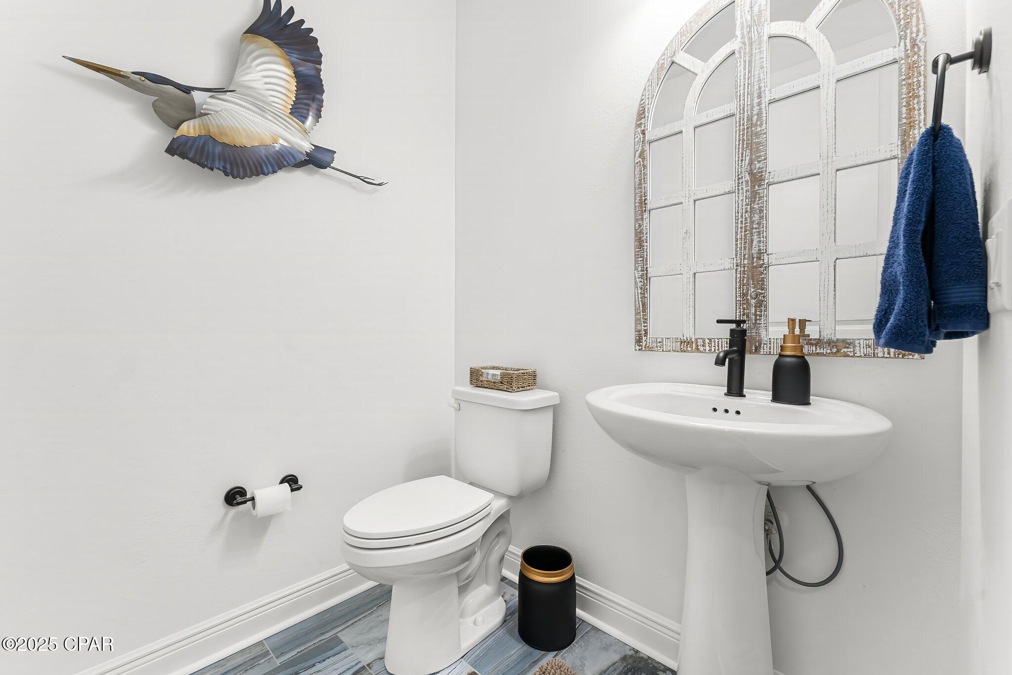 Bright bathroom with a pedestal sink, arched mirror, blue-gray tile floor, and flying-bird wall decoration.
