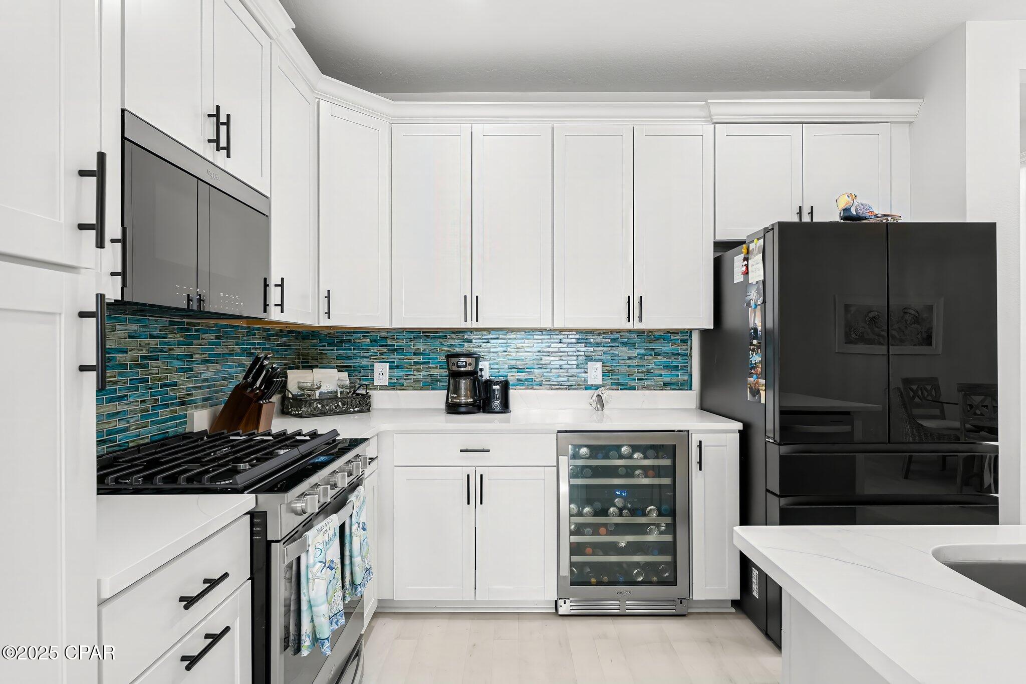 Modern kitchen with white cabinets, blue-green tile backsplash, black appliances, and a wine refrigerator.