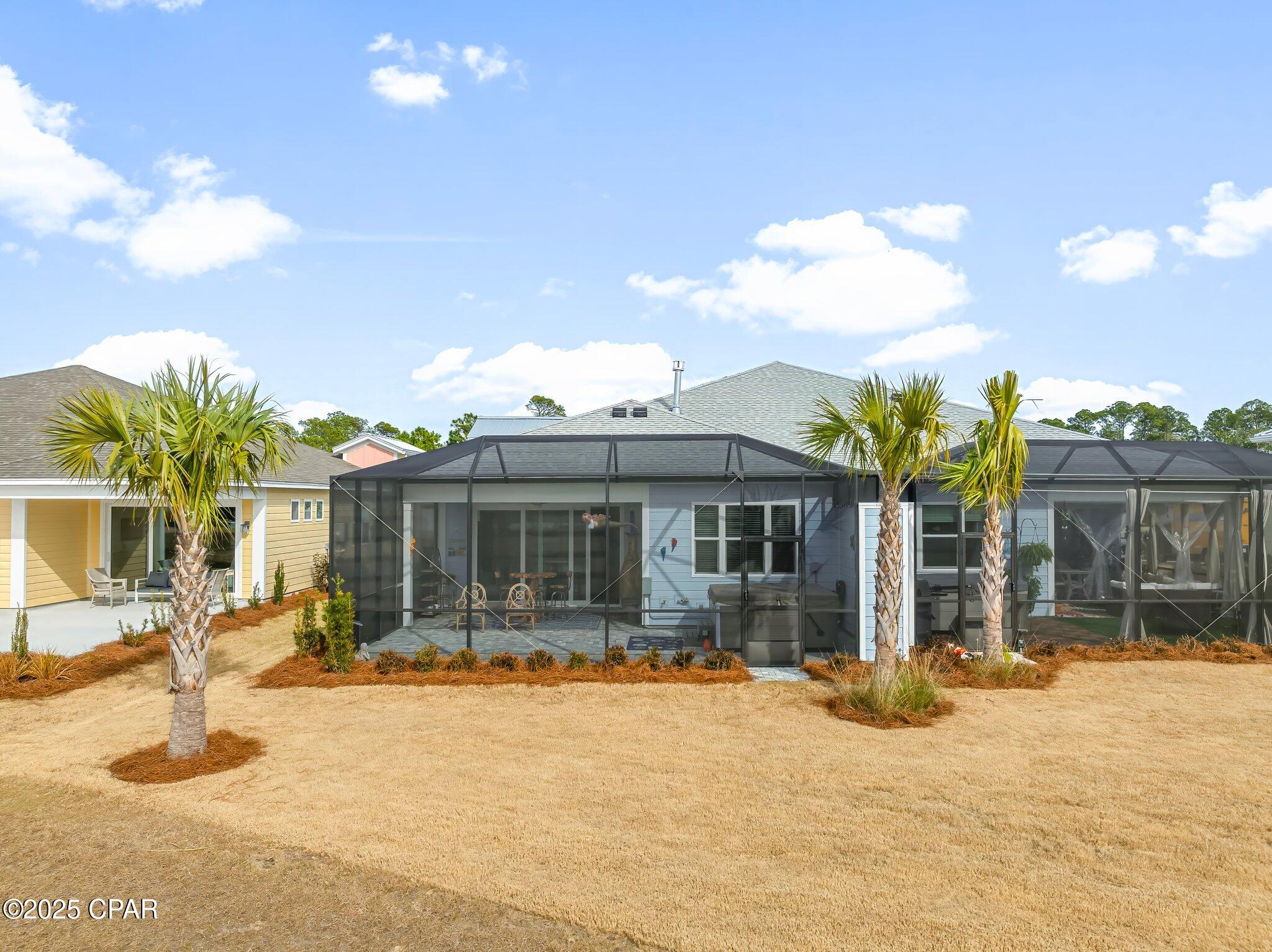 Rear of a light-blue home with a screened patio, palm trees, and a broad lawn.
