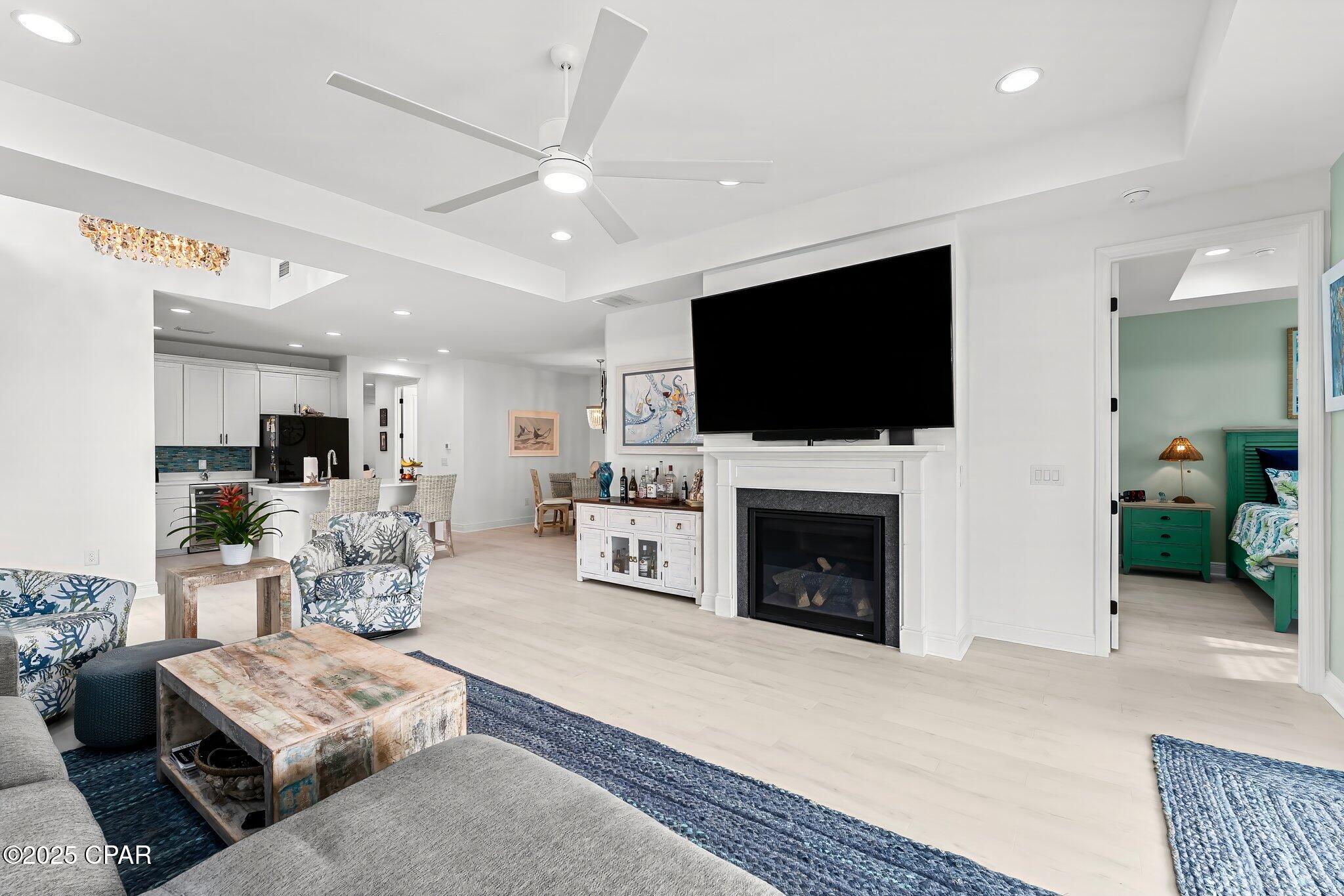 Open-plan living room with a white fireplace and TV, patterned seating, and kitchen beyond.