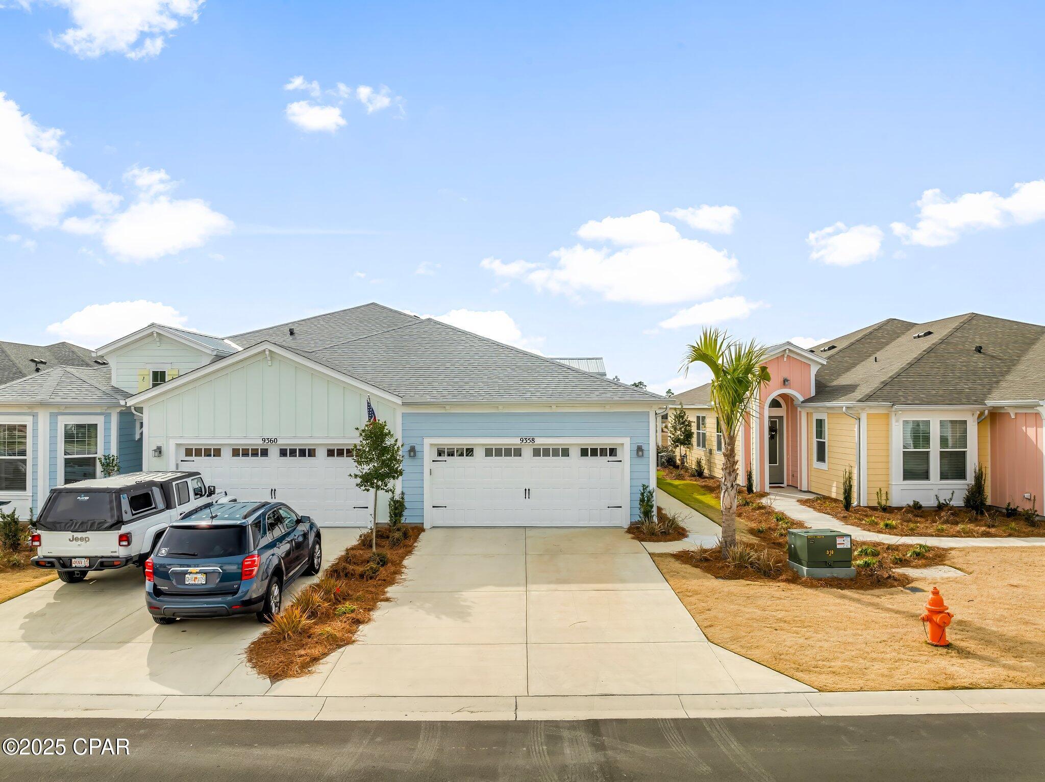 Light blue house with a white double garage, broad driveway, and pastel-colored neighboring homes.