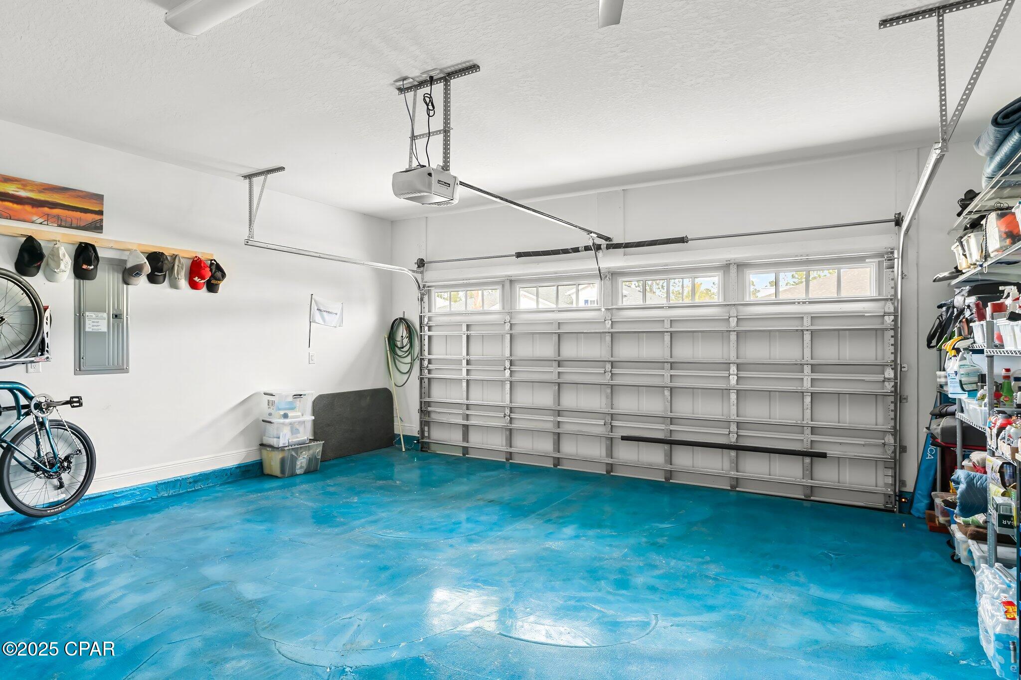 Garage with a vivid blue floor, wide paneled door, bicycles, and storage shelves.