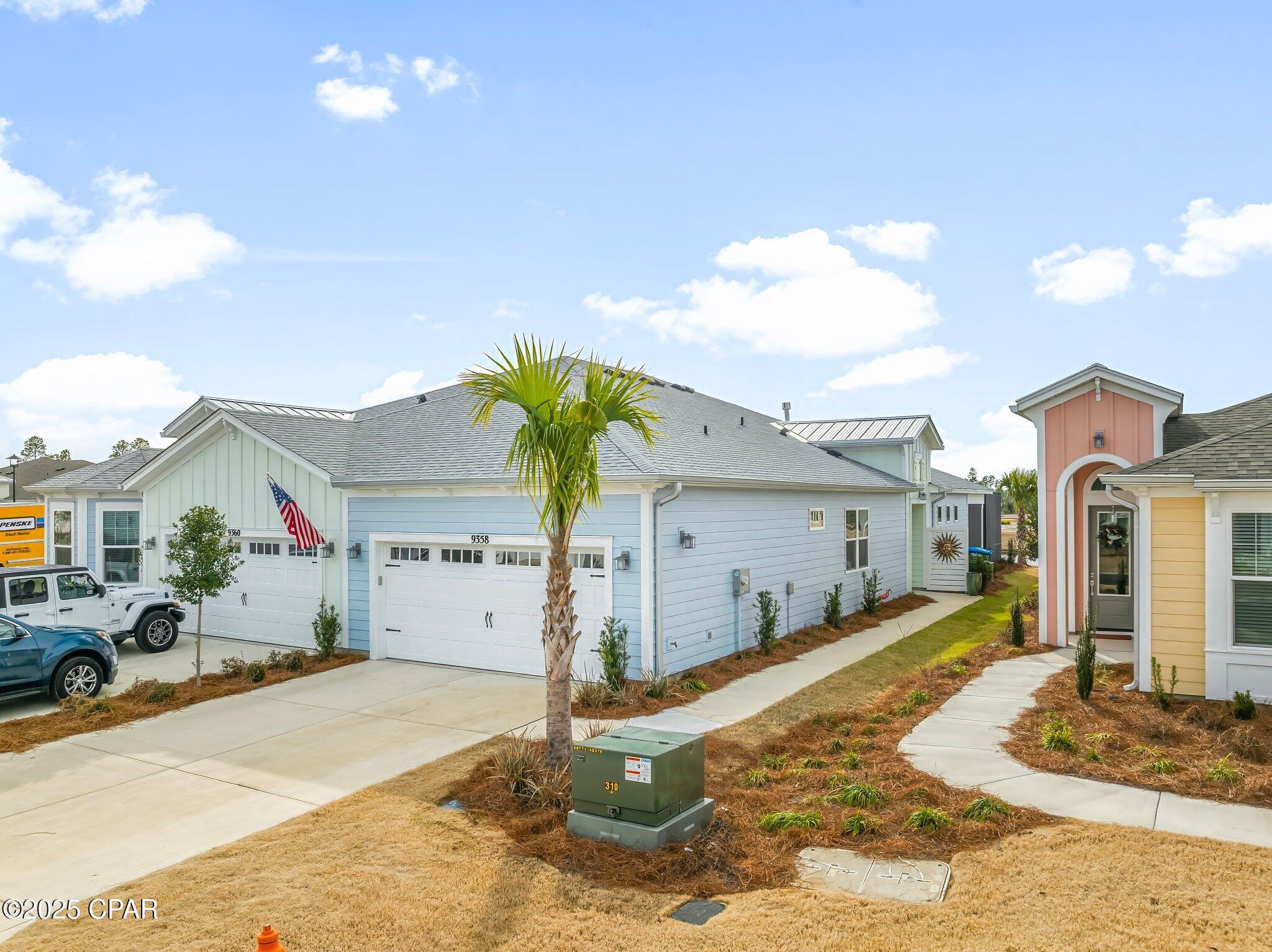 Light blue home with a wide garage, palm tree, and neighboring pastel-colored houses.