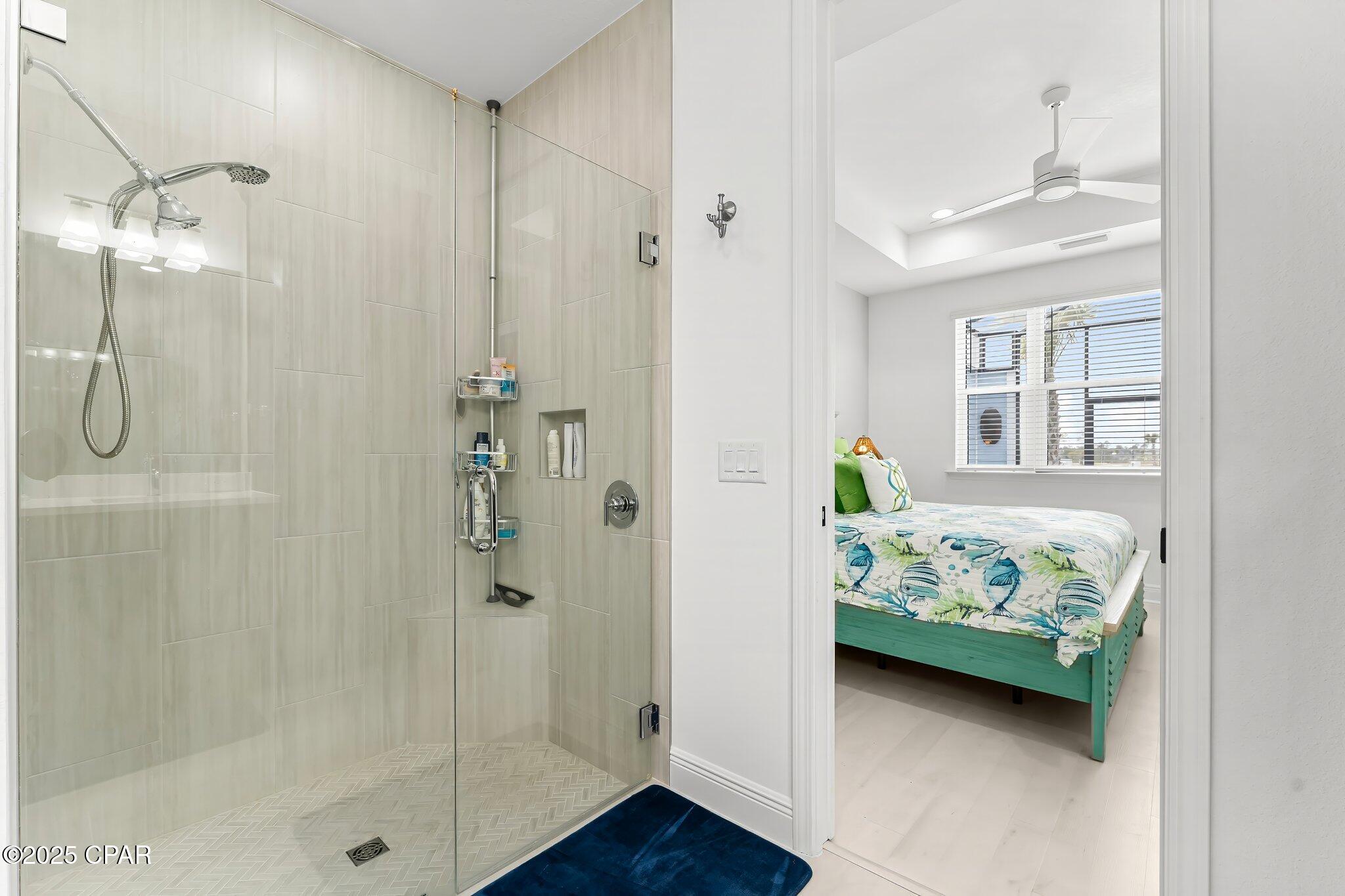 Bathroom with a glass walk-in shower and doorway to a bedroom with fish-patterned bedding.