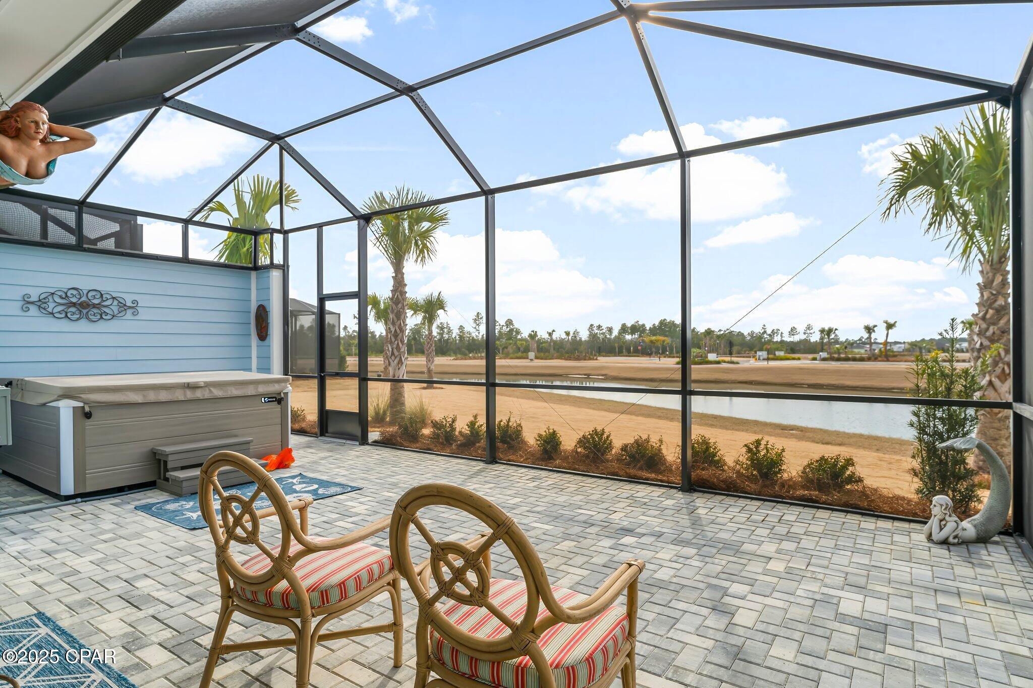 Screened patio with a hot tub and cushioned chairs overlooking a pond.