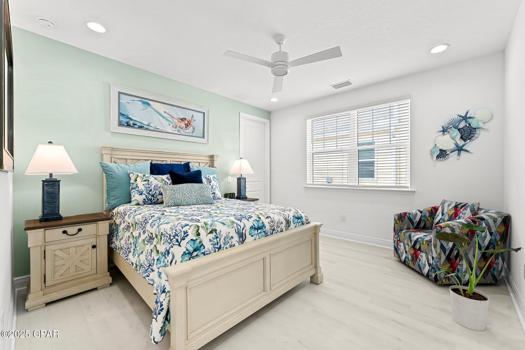 Bedroom with a cream bed, blue floral bedding, mint-green accent wall, and coastal decorations.