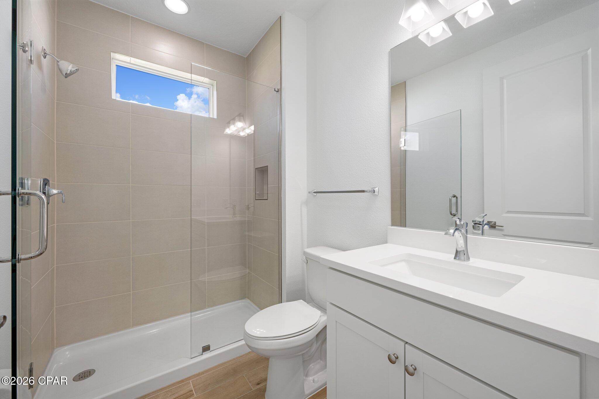 Bathroom with glass-enclosed tiled shower, high window, and white vanity.