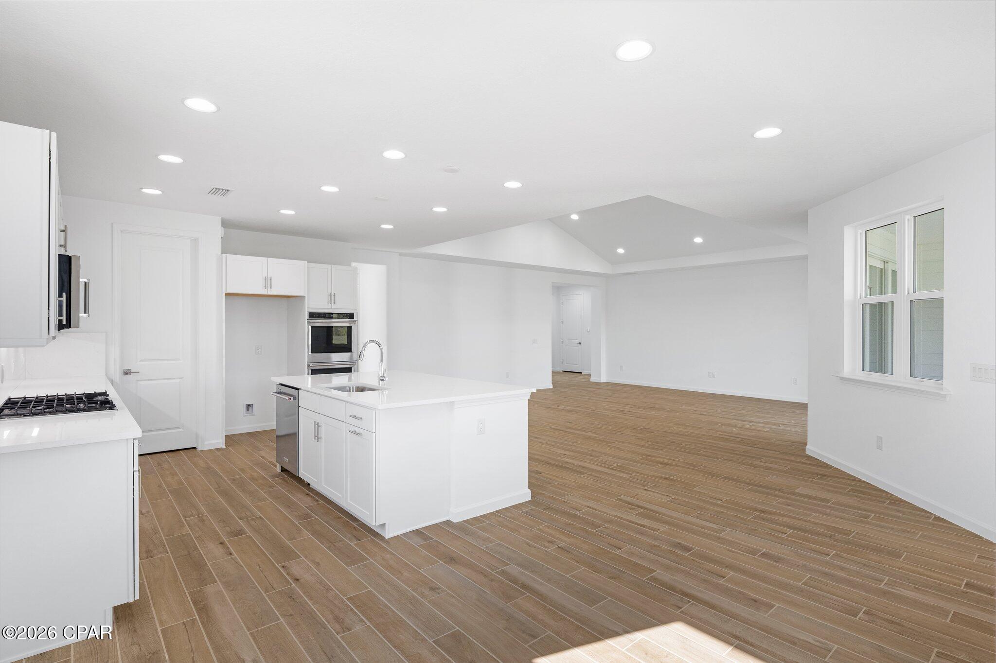 Open-plan kitchen and living area with a white island, wood-look tile floors, and large windows.