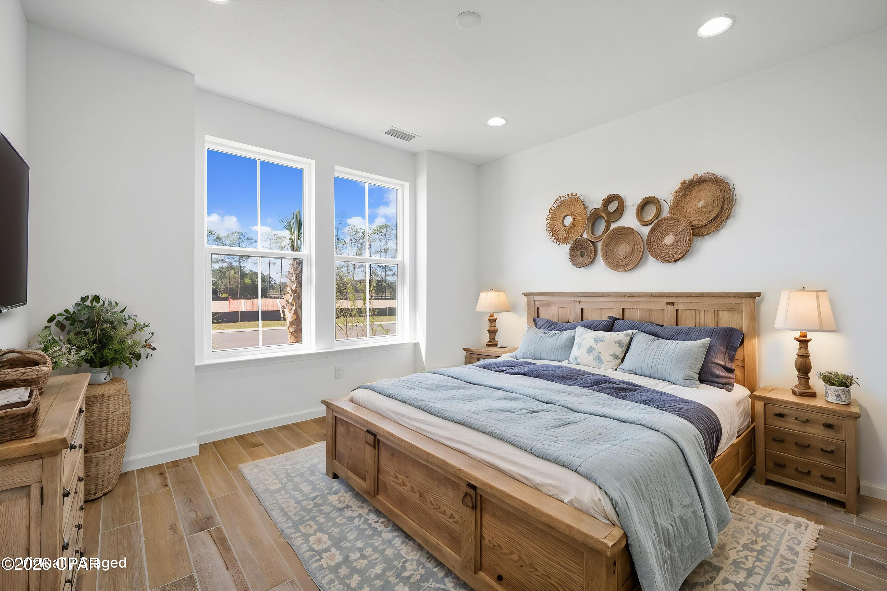 Furnished bedroom with a wooden bed, woven wall decor, and two large windows.