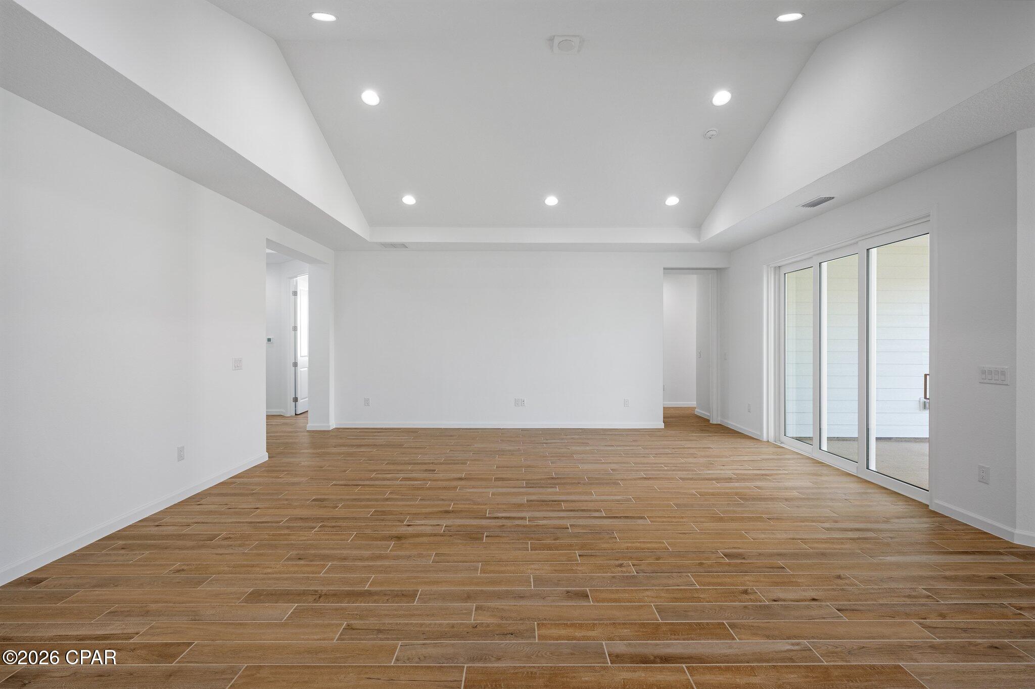 Empty living area with wood-look tile floors, high ceiling, and large sliding glass doors.