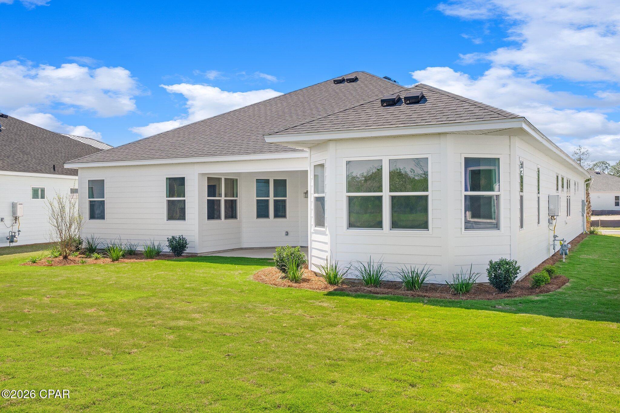 White-sided home with a gray hip roof, covered rear patio, landscaped beds, and a broad lawn.