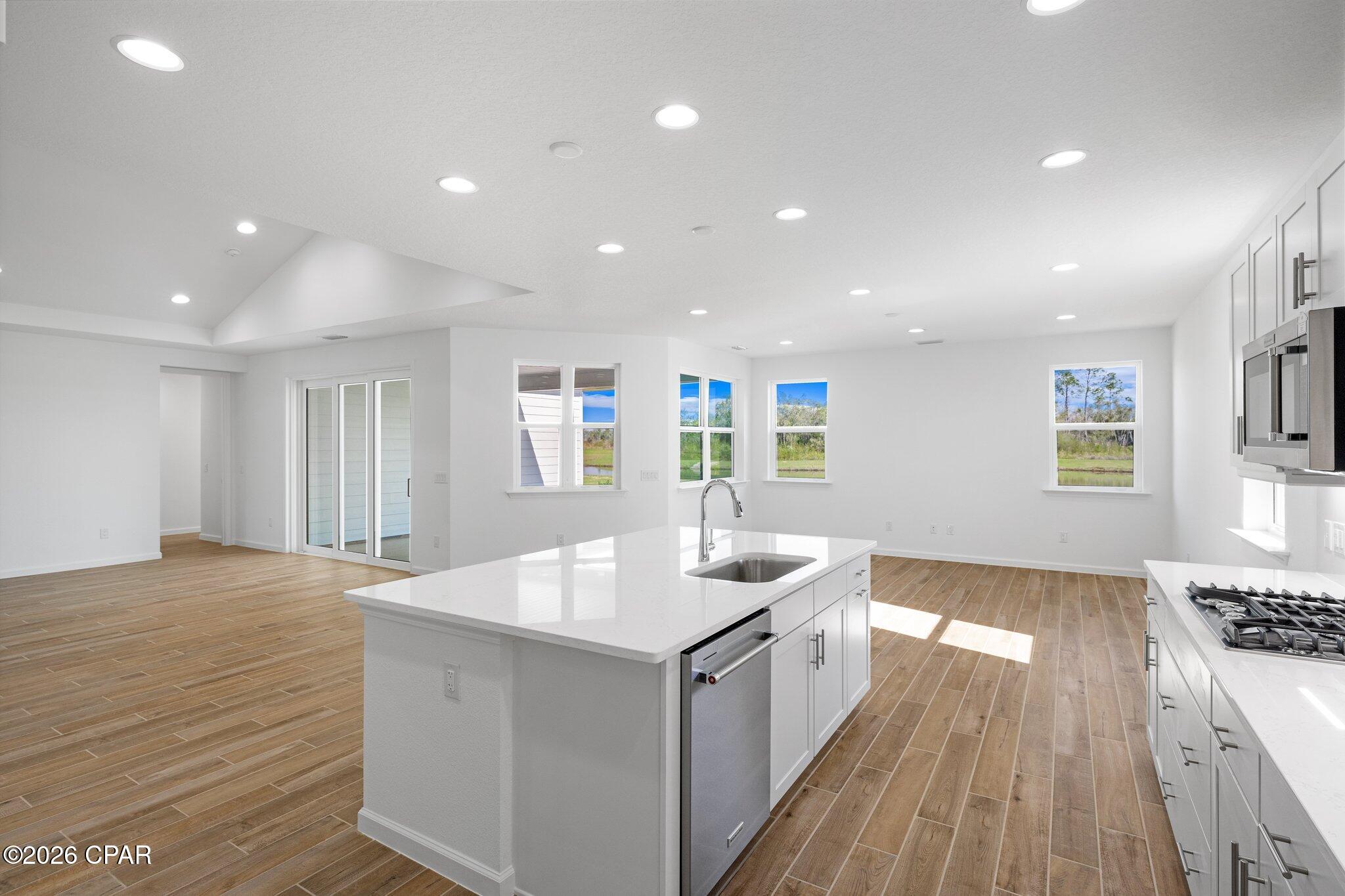 Open kitchen with a large white island, stainless steel appliances, and wood-look tile flooring.