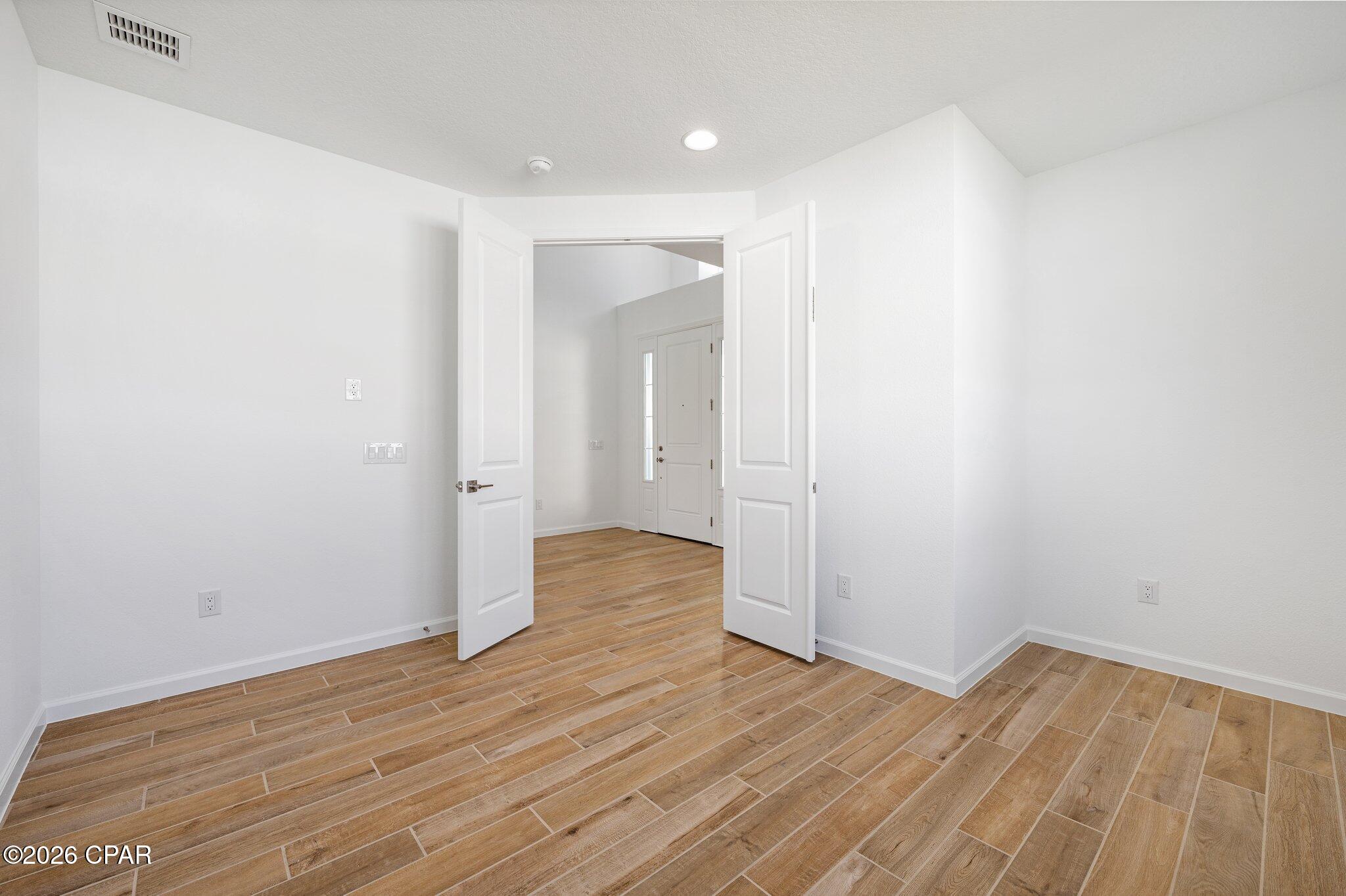 Empty interior room with wood-look tile flooring and open double doors to the entry hall.