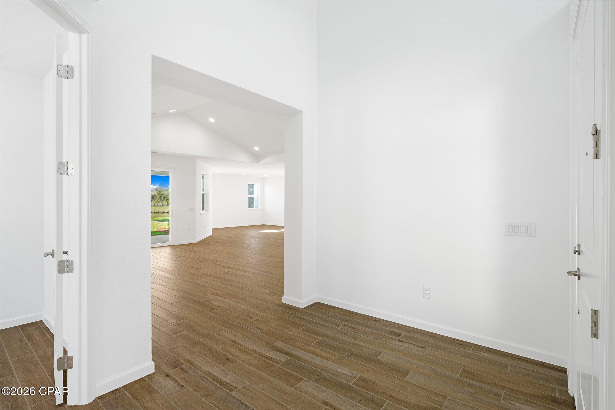 Empty white interior with brown tile flooring and an open doorway to a vaulted room.