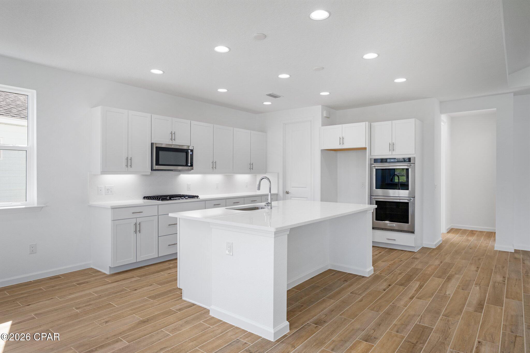 Vacant kitchen with a large white island, stainless appliances, and wood-look tile flooring.