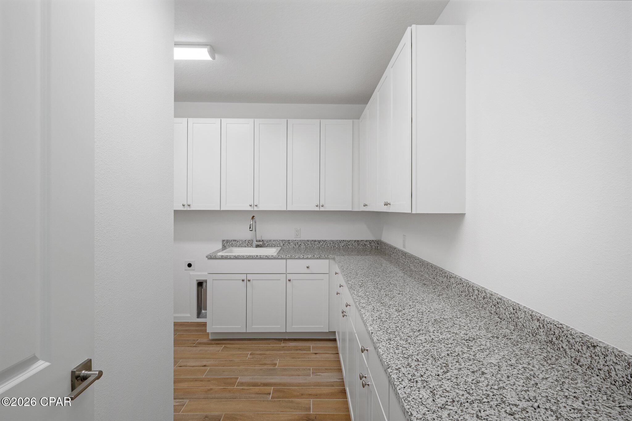 Laundry room with white cabinets, granite counters, a utility sink, and wood-look tile flooring.