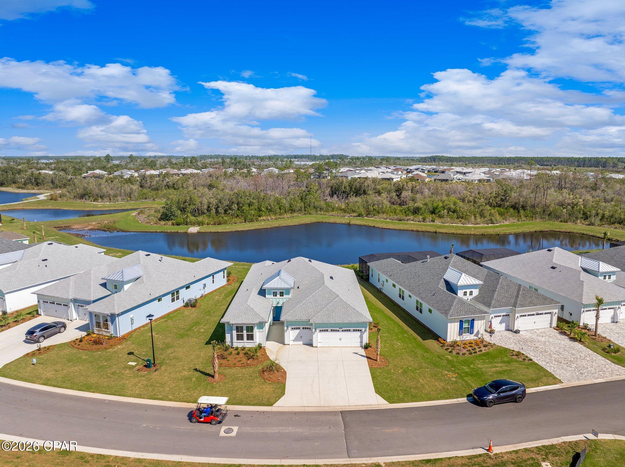 Aerial view of a single-story home facing a pond, with neighboring homes and a curved street.