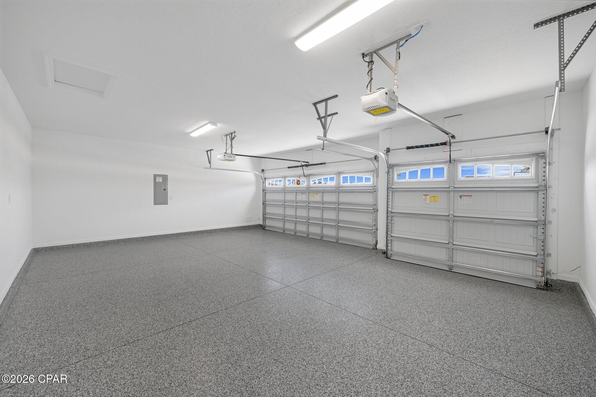 Empty two-car garage with speckled flooring and two windowed overhead doors.