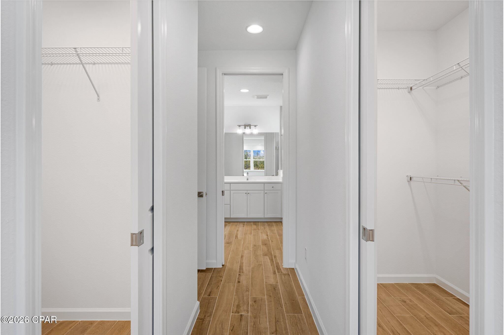 Empty hallway with wood-look flooring, open closets on both sides, and a bathroom vanity at the far end.