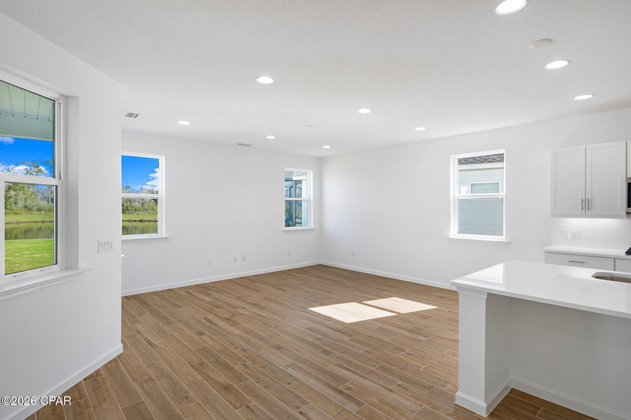 Vacant kitchen and dining area with wood-look tile floors, white island, and large windows.