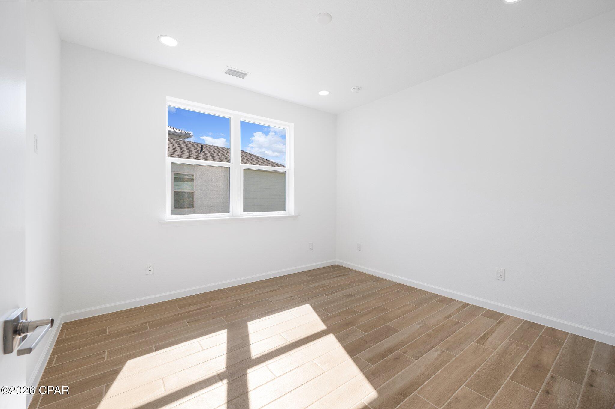Vacant room with wood-look tile flooring and a sunlit window.