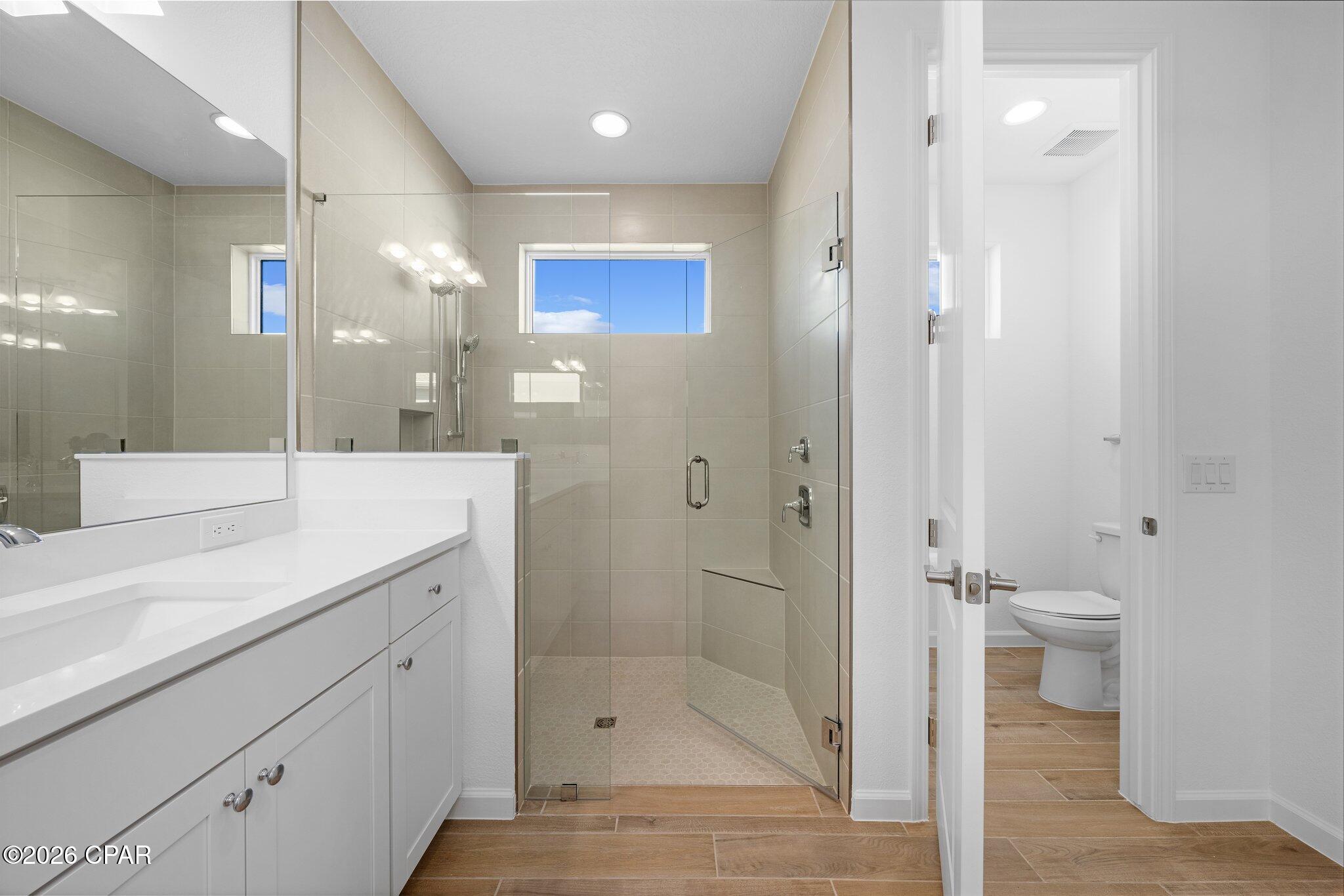 Bathroom with a glass walk-in shower, white vanity, and doorway to a separate toilet room.
