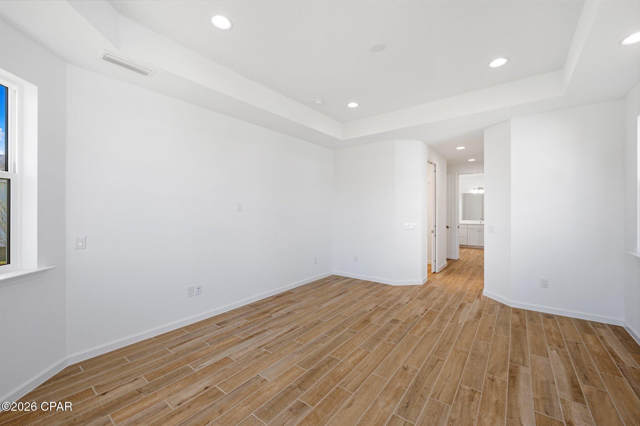 Empty bedroom with wood-look tile floors, a tray ceiling, and a doorway to the bathroom.