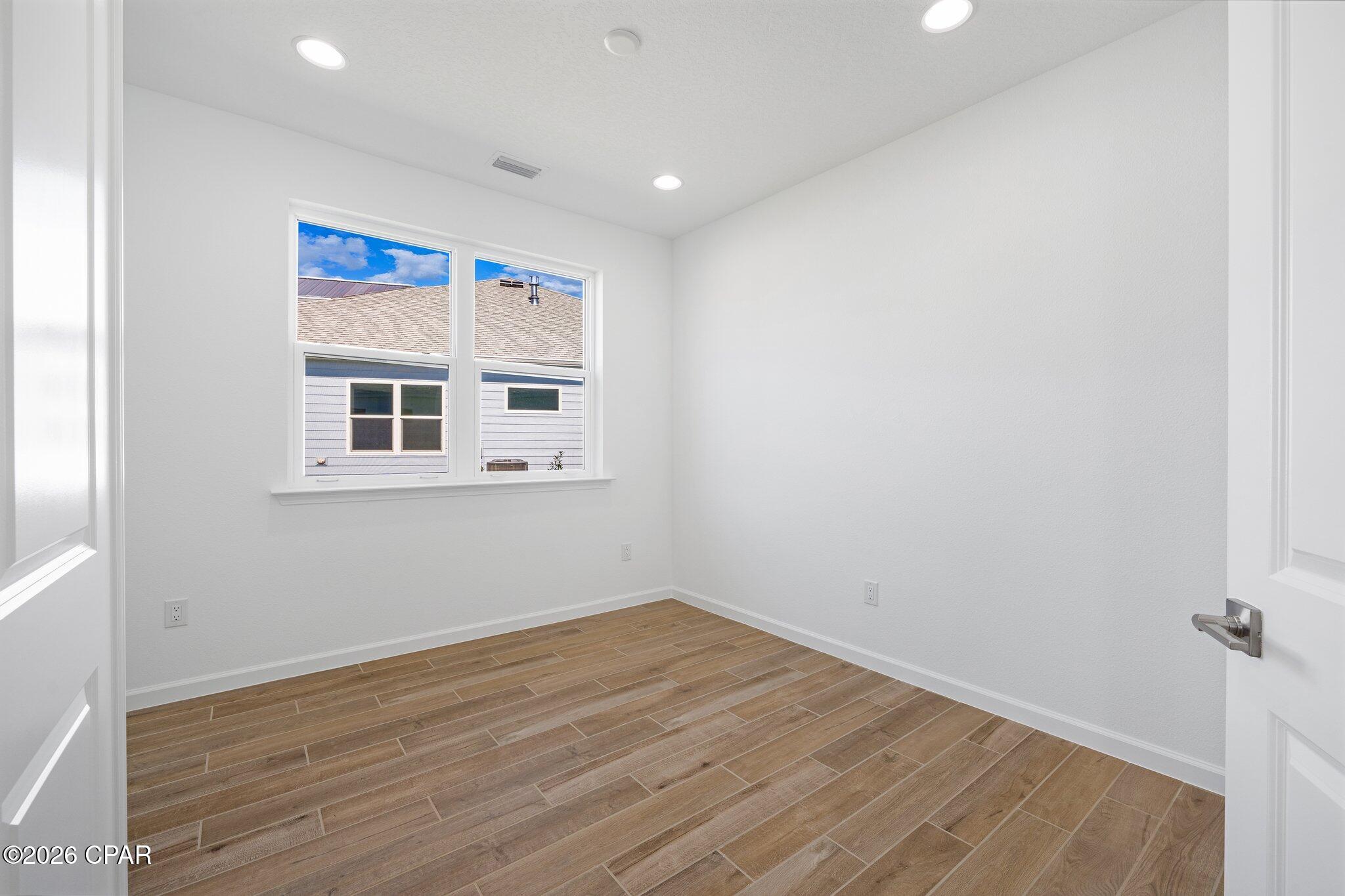 Empty room with wood-look tile flooring and two windows.