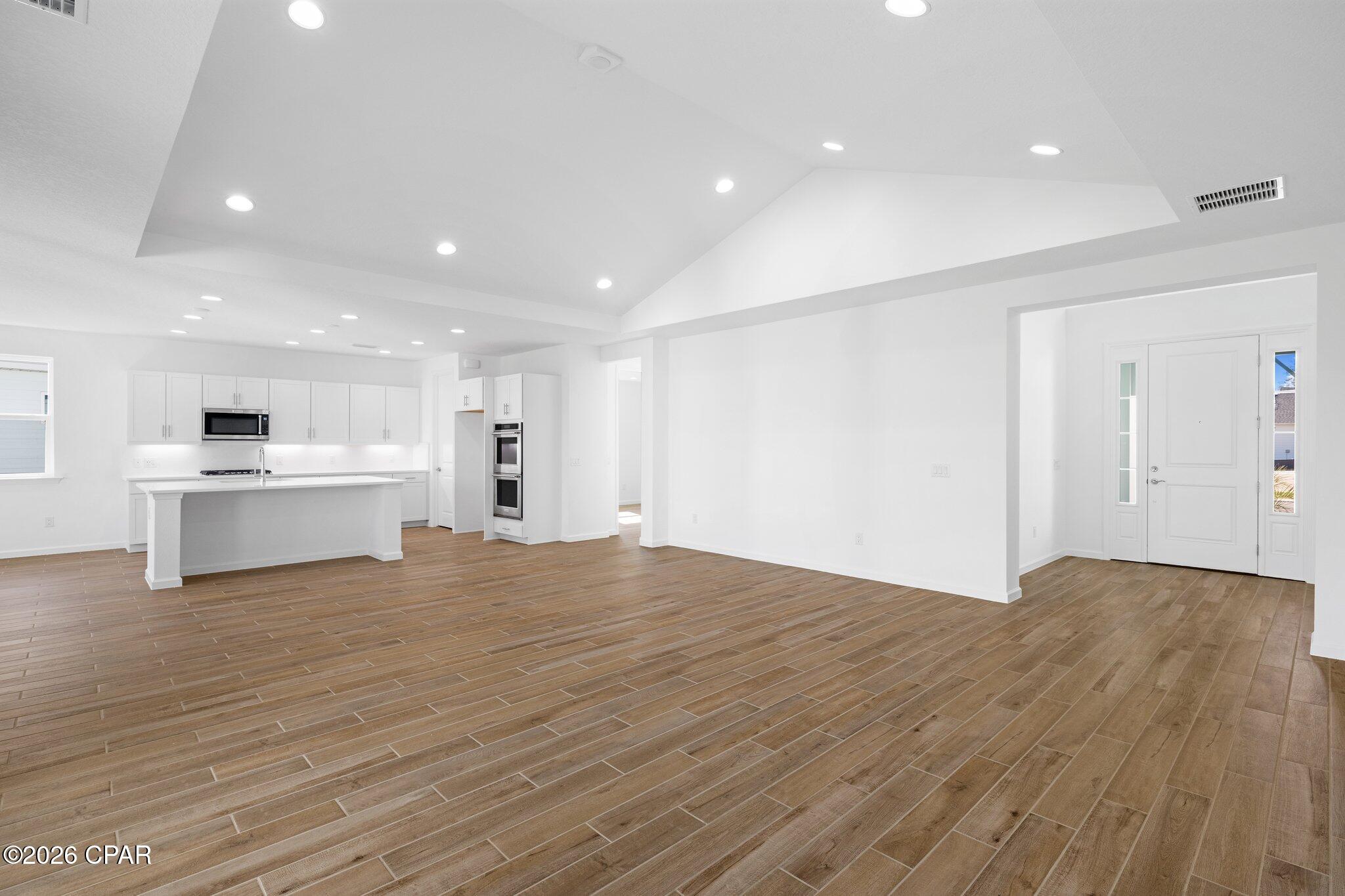 Open kitchen and entry with white cabinetry, a large island, and wood-look tile flooring.